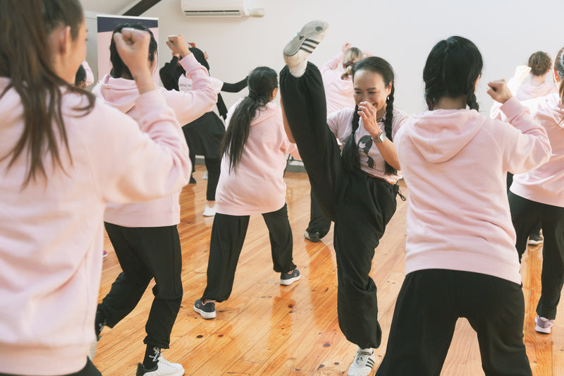 Group of people in pink hoodies and black pants performing self defence in a room with wooden floors at RMIT University