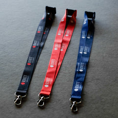 Three RMIT Lanyards in black, red, and navy blue lie flat side-by-side on a light grey fabric surface, each featuring repeated white RMIT University logo prints along the woven polyester strap, a black plastic safety breakaway clip at the top, and a silver metal swivel lobster clasp at the end, as shown in this product image available from the RMIT Store.