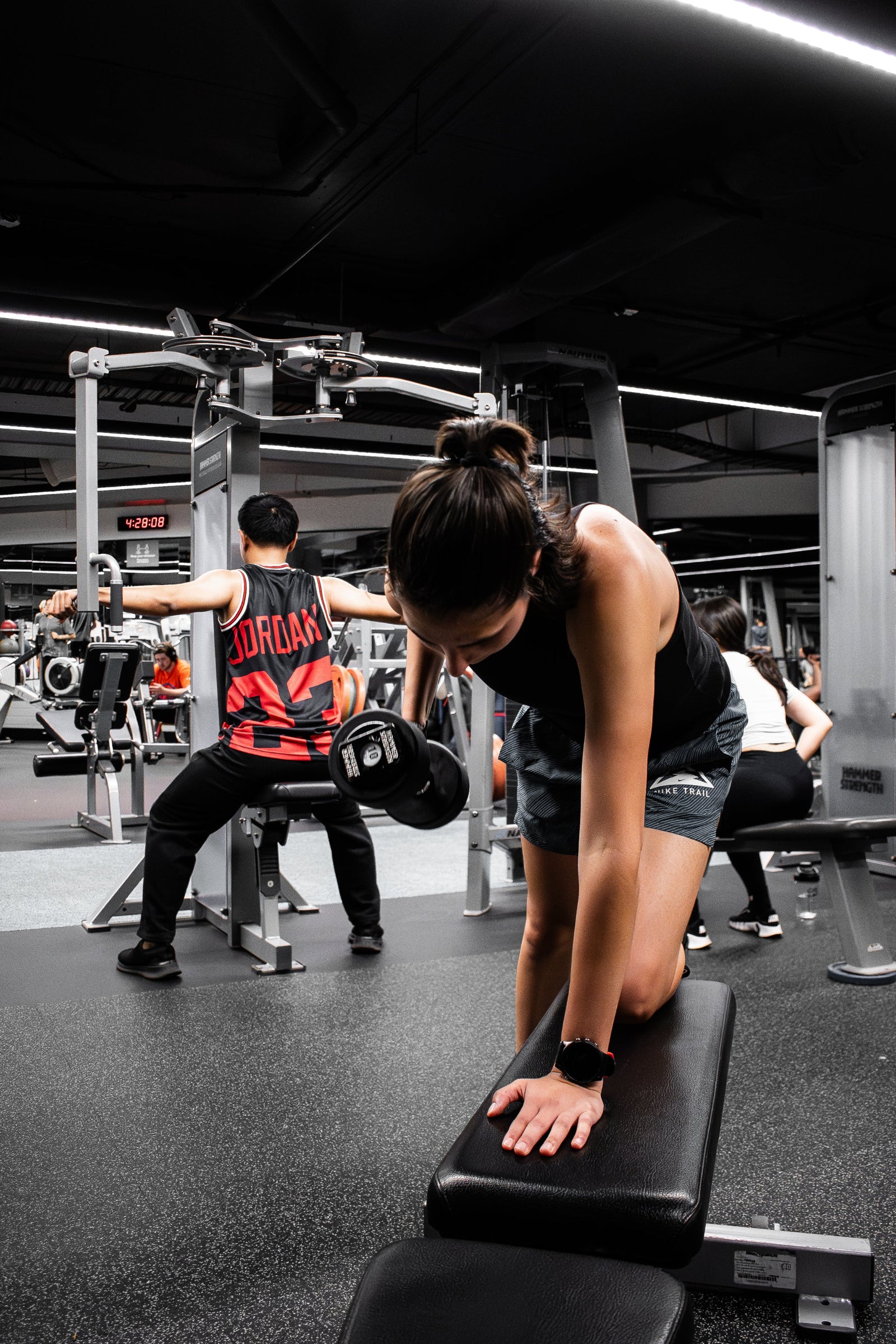 Woman performing single arm dumbbell rows in the RMIT Active Hub with people in the background exercising at RMIT University