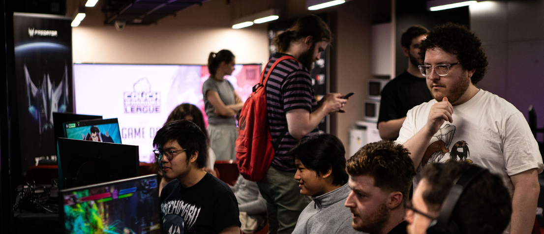 Group of people gathered in a room playing video games, with multiple monitors and gaming equipment at RMIT Games Hub for RMIT Games Day.