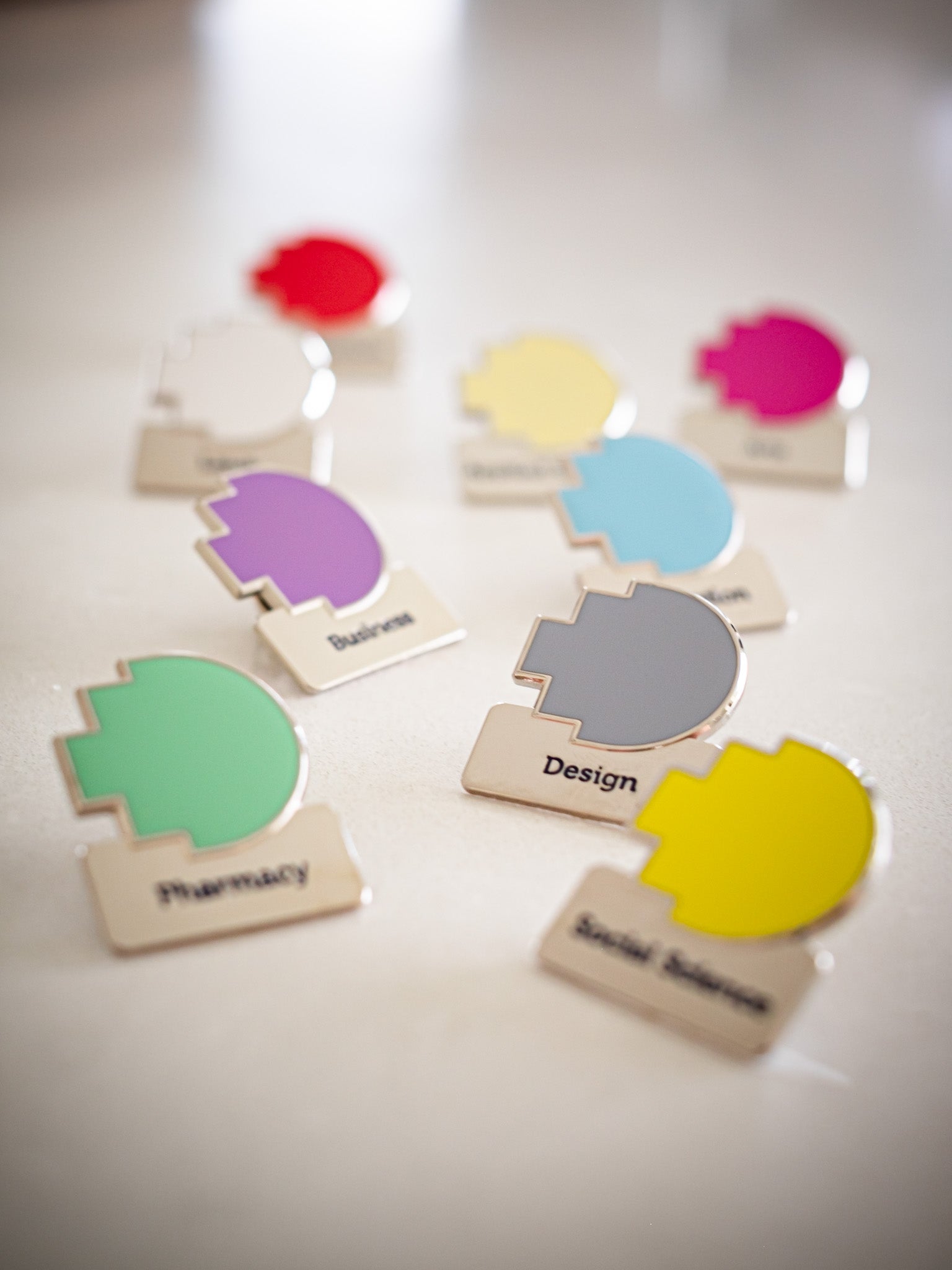 Group photo of nine RMIT discipline pins scattered on a light marble background, showing various coloured pixelated logos and silver squares with discipline names, available at the RMIT Store.