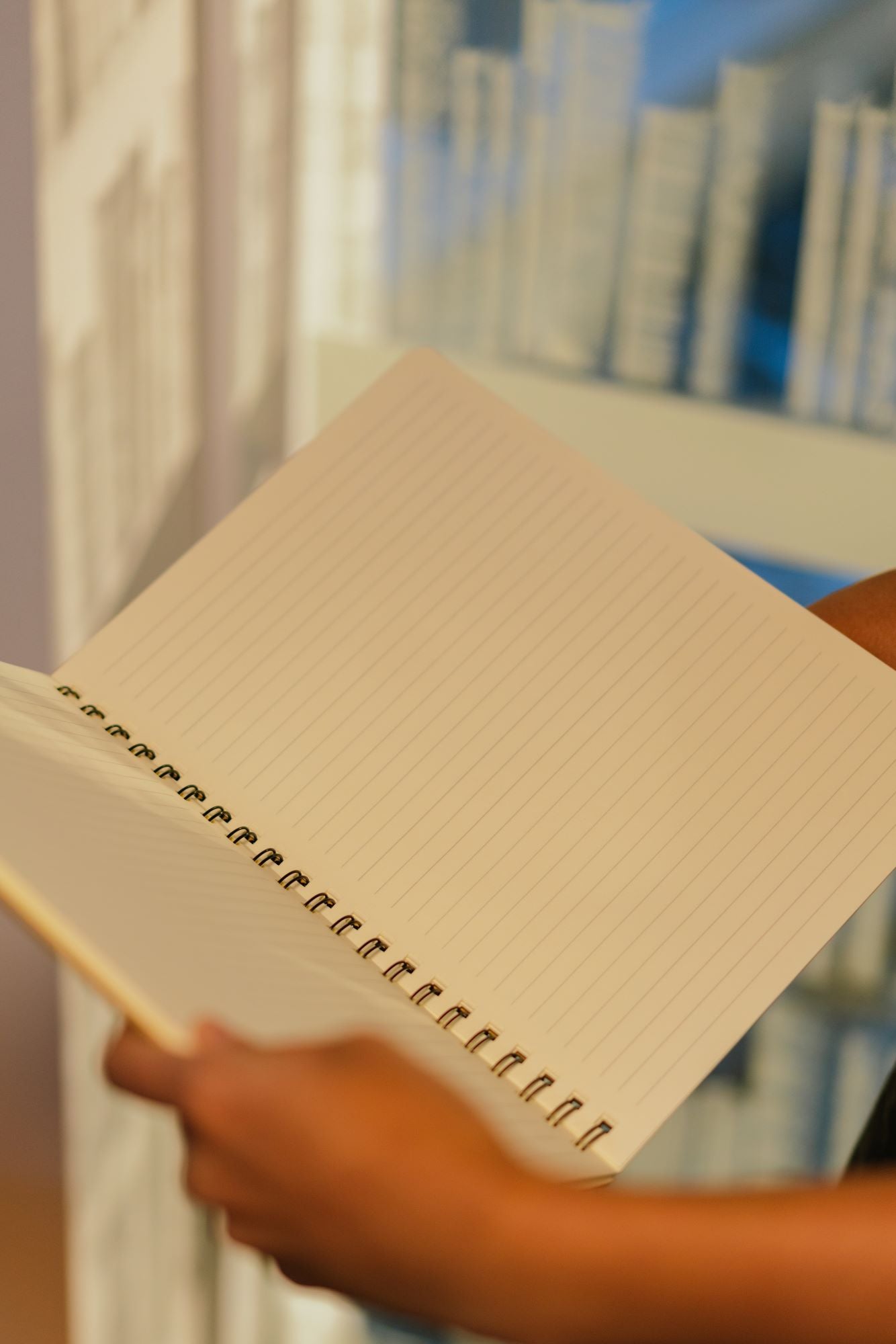 A model holding an open A4-sized recycled notebook from the RMIT Store, showing lined cream-coloured pages. The notebook has a brown kraft paper cover and is held with both hands against a plain background. The visible pages have clear horizontal lines and a subtle texture.