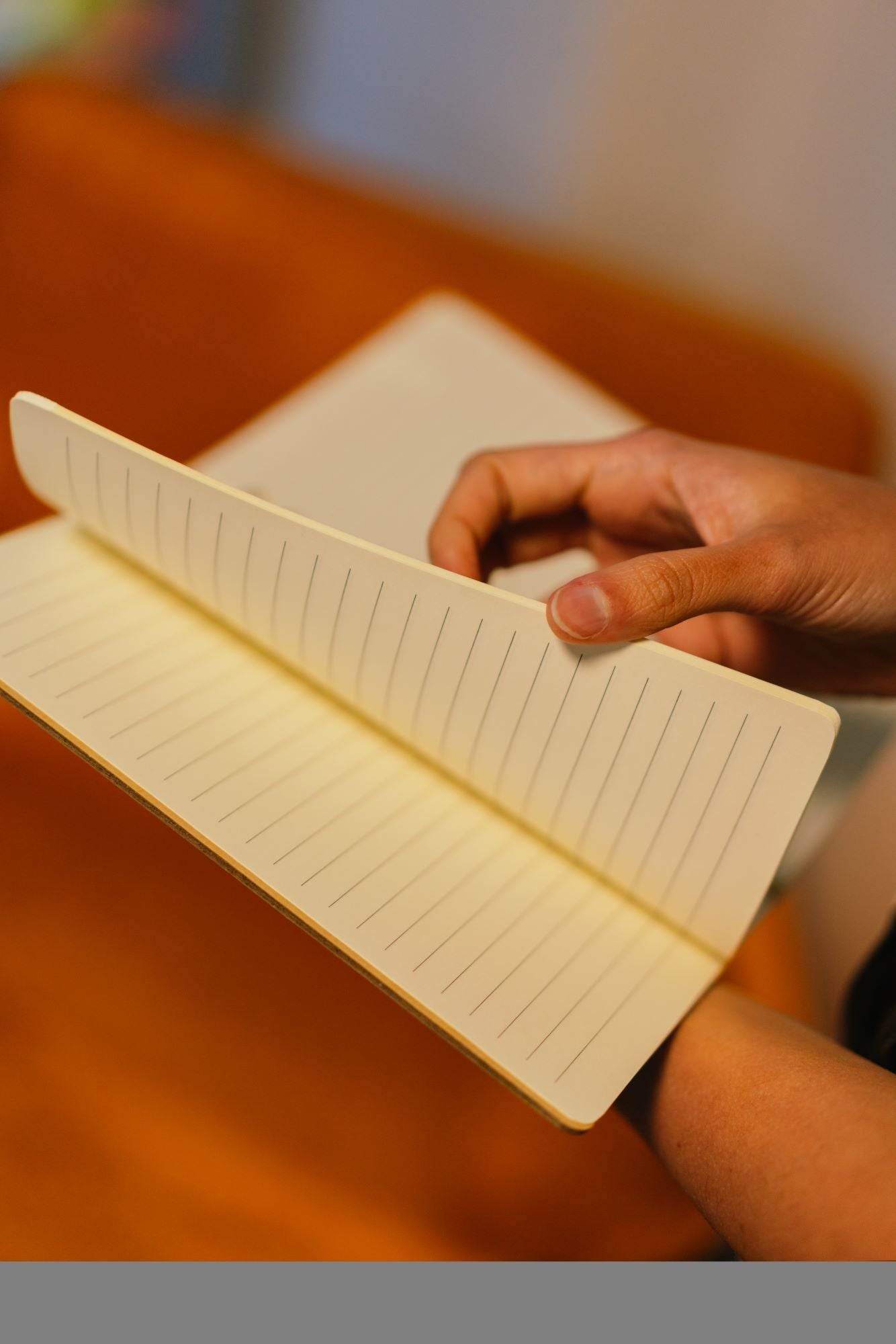 RMIT Store A5 Recycled Notebook shown open from a side view on a wooden tabletop, with a model’s hand lifting several lined pages. 