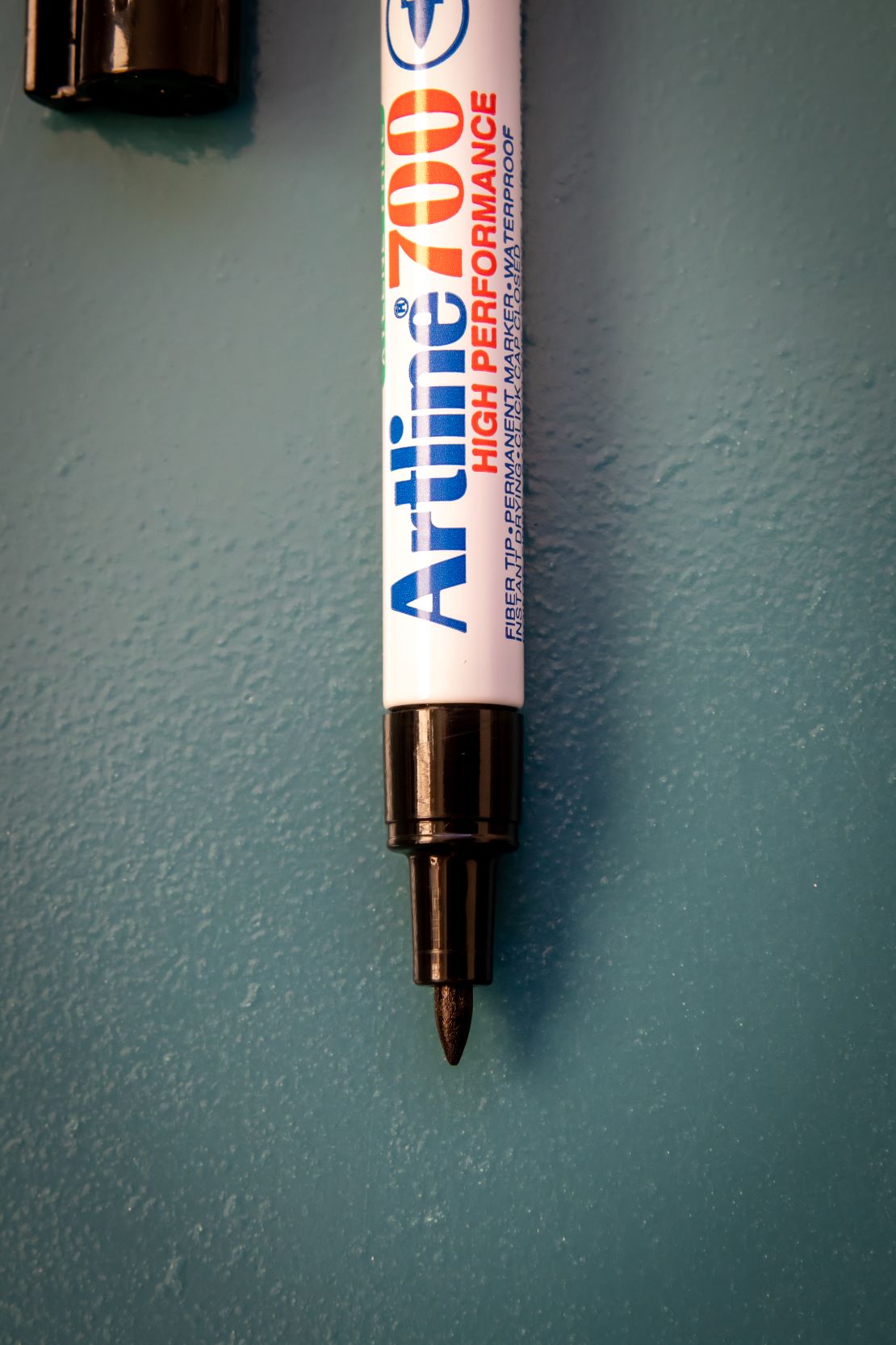 Artline 700 high-performance permanent marker with a fine fiber tip, displayed vertically against a blue background.