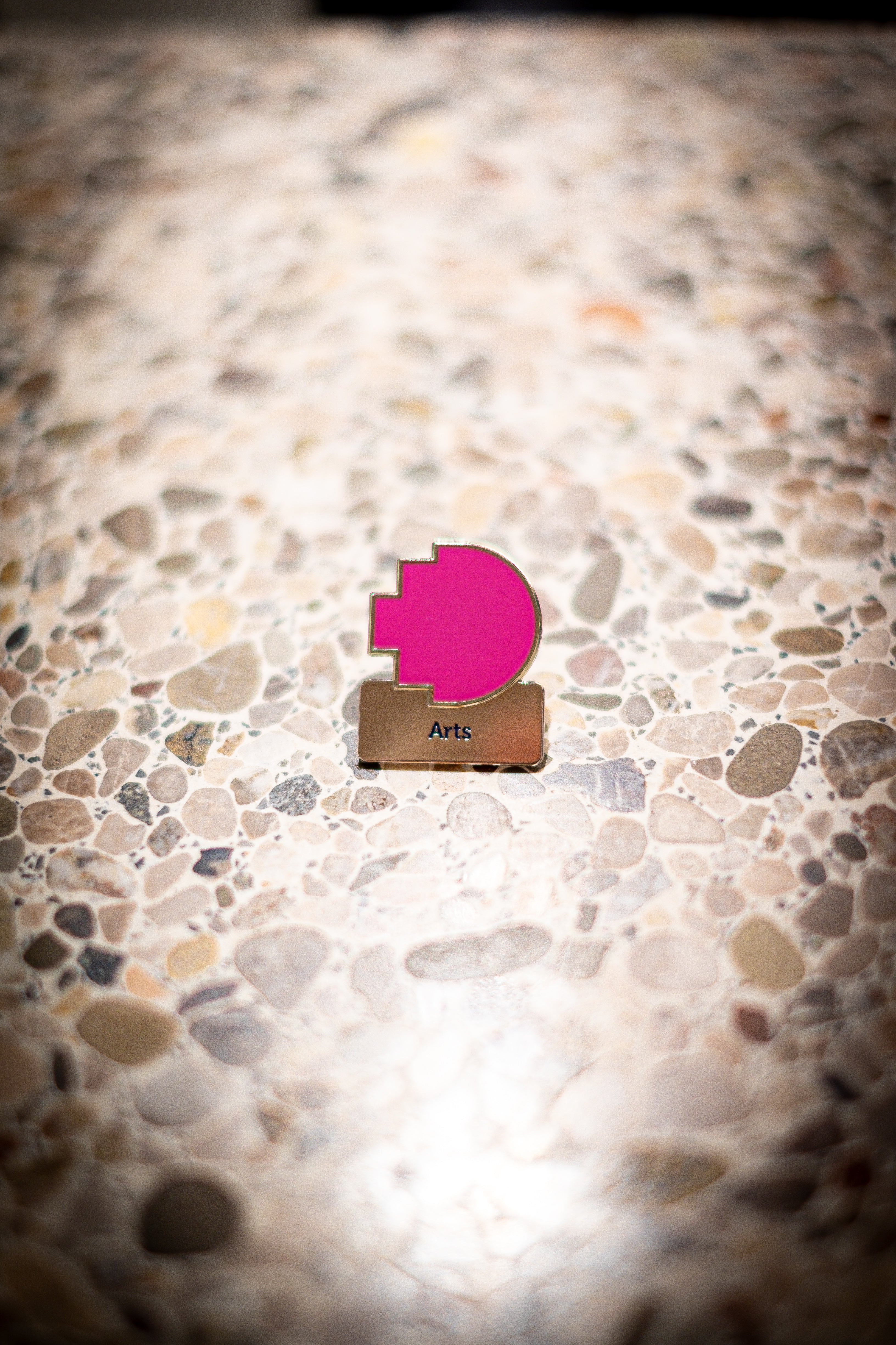 Arts discipline pin featuring a magenta pixelated logo above a silver square with 'Arts' text, positioned on a light marble background, available at the RMIT Store.