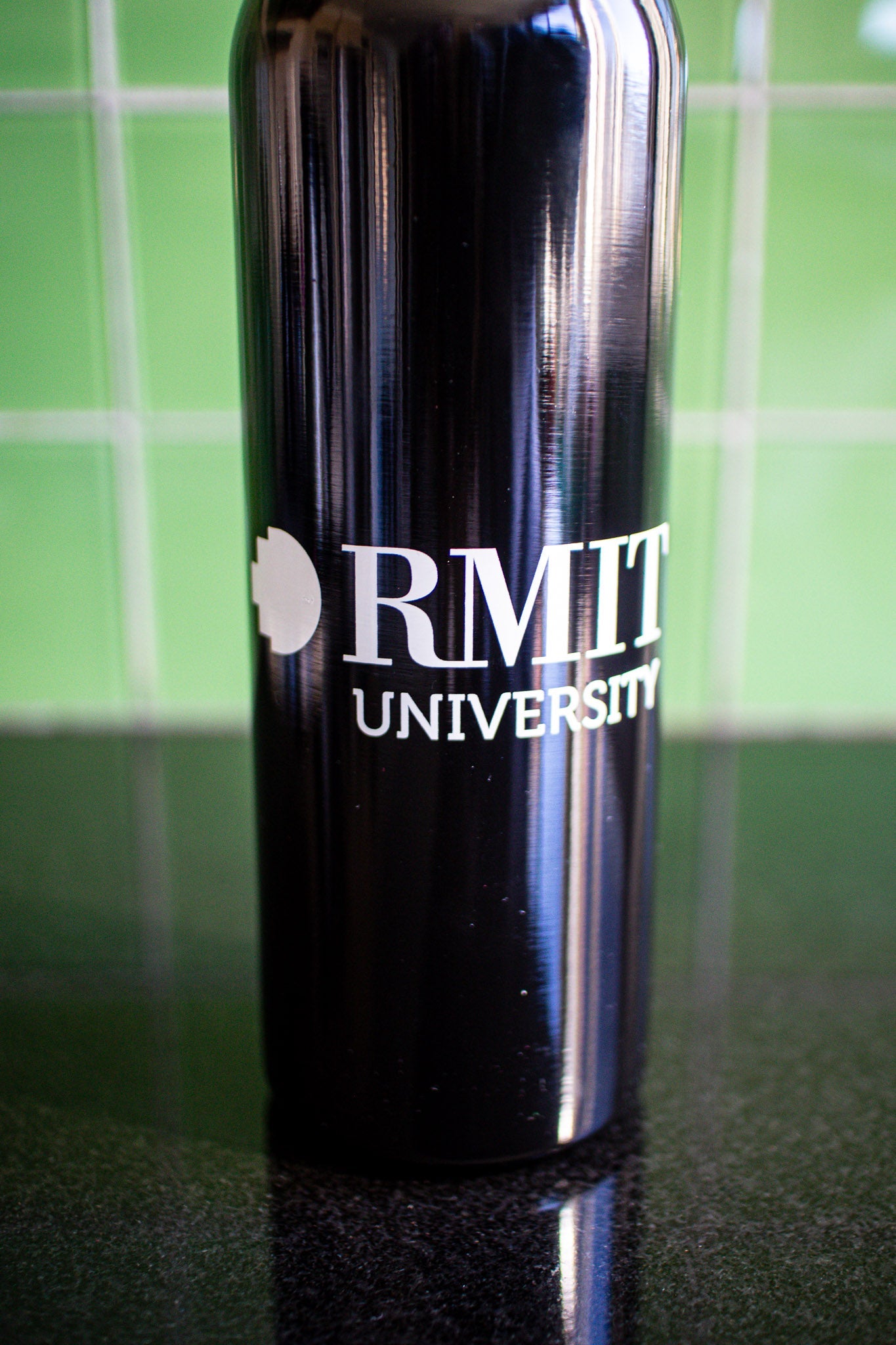 Close-up view of the black RMIT bottle, featuring a centrally placed white RMIT University logo on the bottle’s body. Available at the RMIT Store.