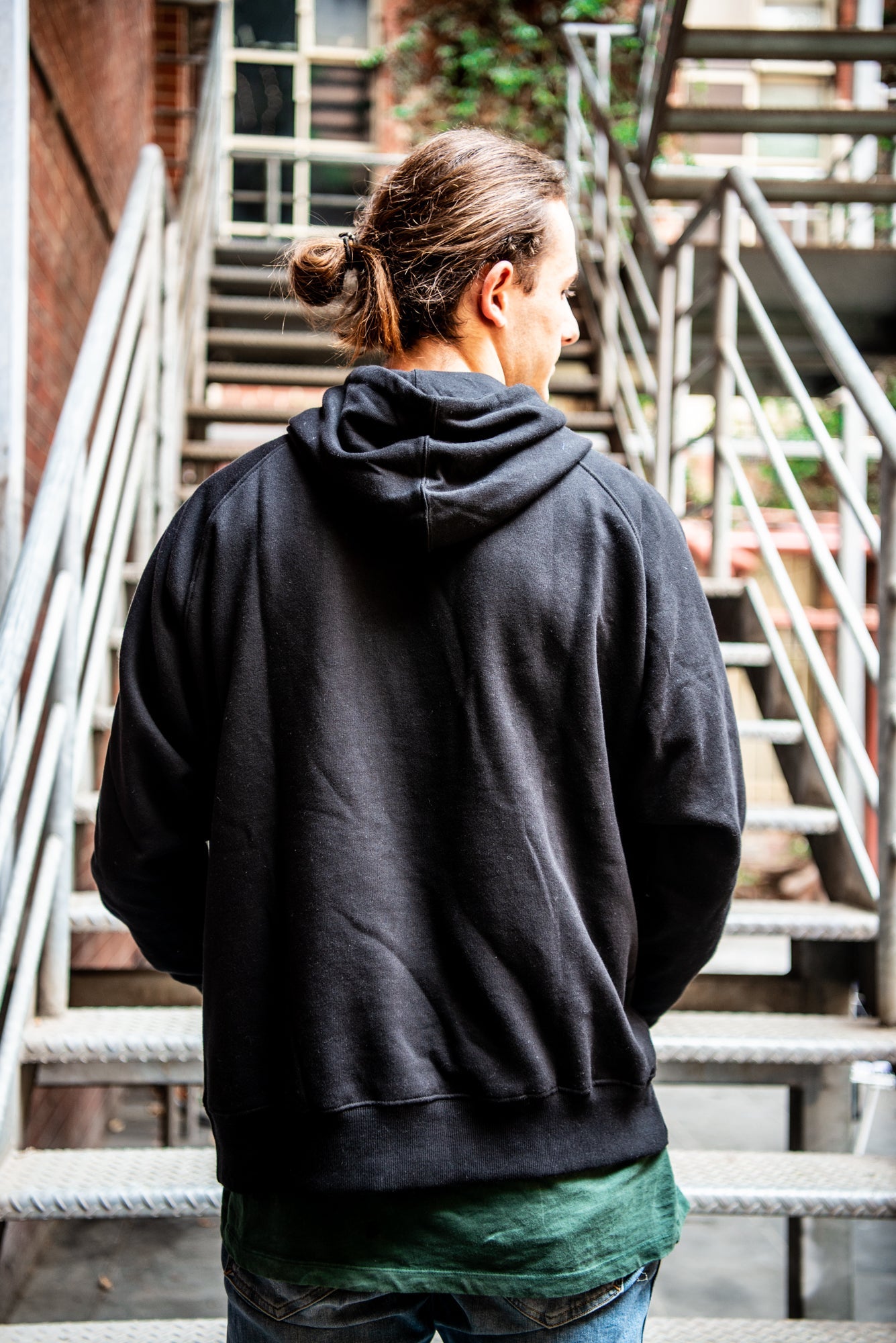 Back view of the black Fairtrade hoodie from the RMIT Store, showing the plain fabric with no visible logos or prints. The hoodie has a relaxed fit, a hood hanging down, and is photographed on a neutral background.