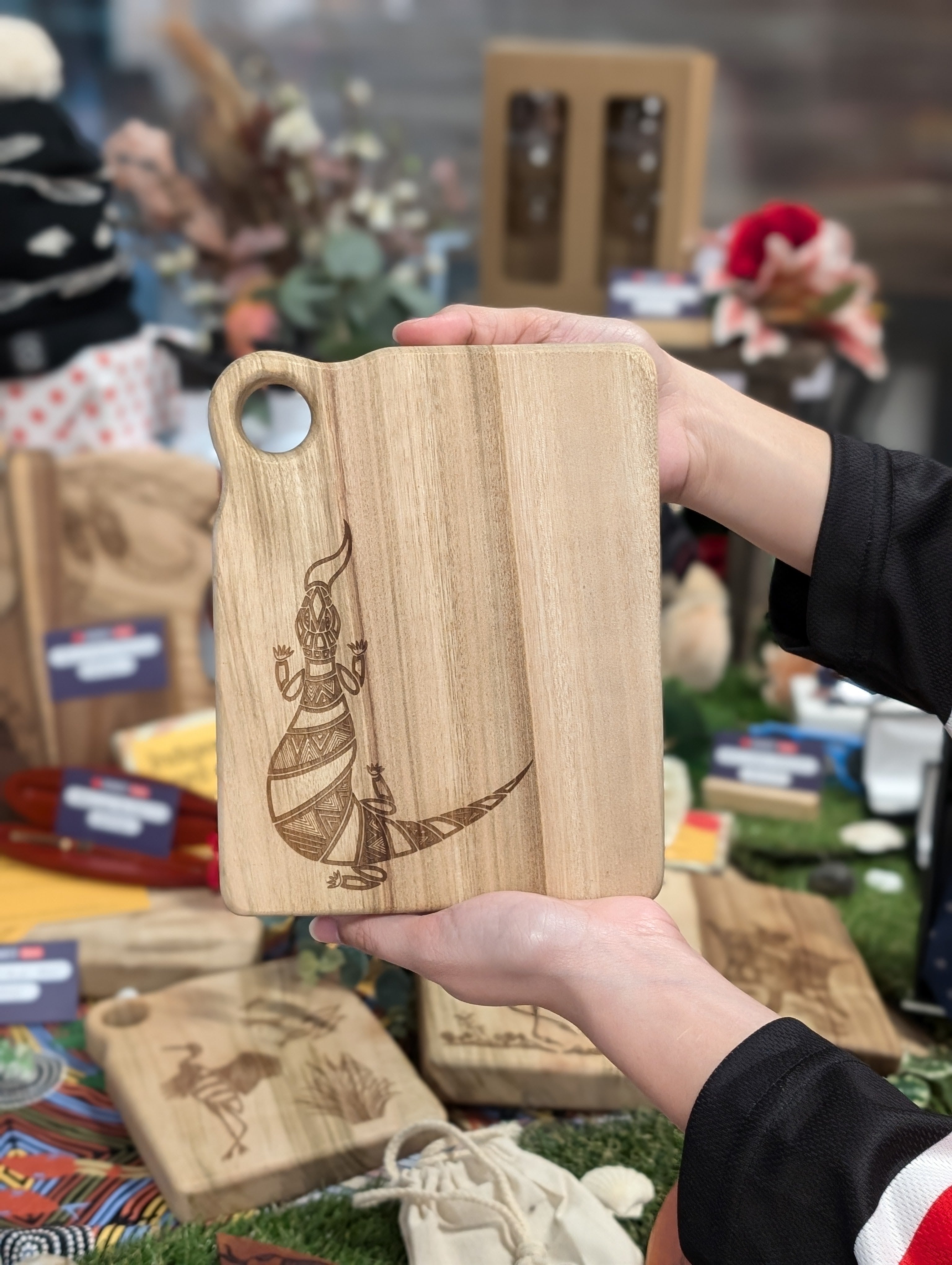 RMIT Store Camphor Laurel Board Extra Mini Rectangle held by a person's hands, featuring an intricately engraved pattern of Bili the Bluetongue Lizard, with a smooth finish and a circular hole for easy hanging.