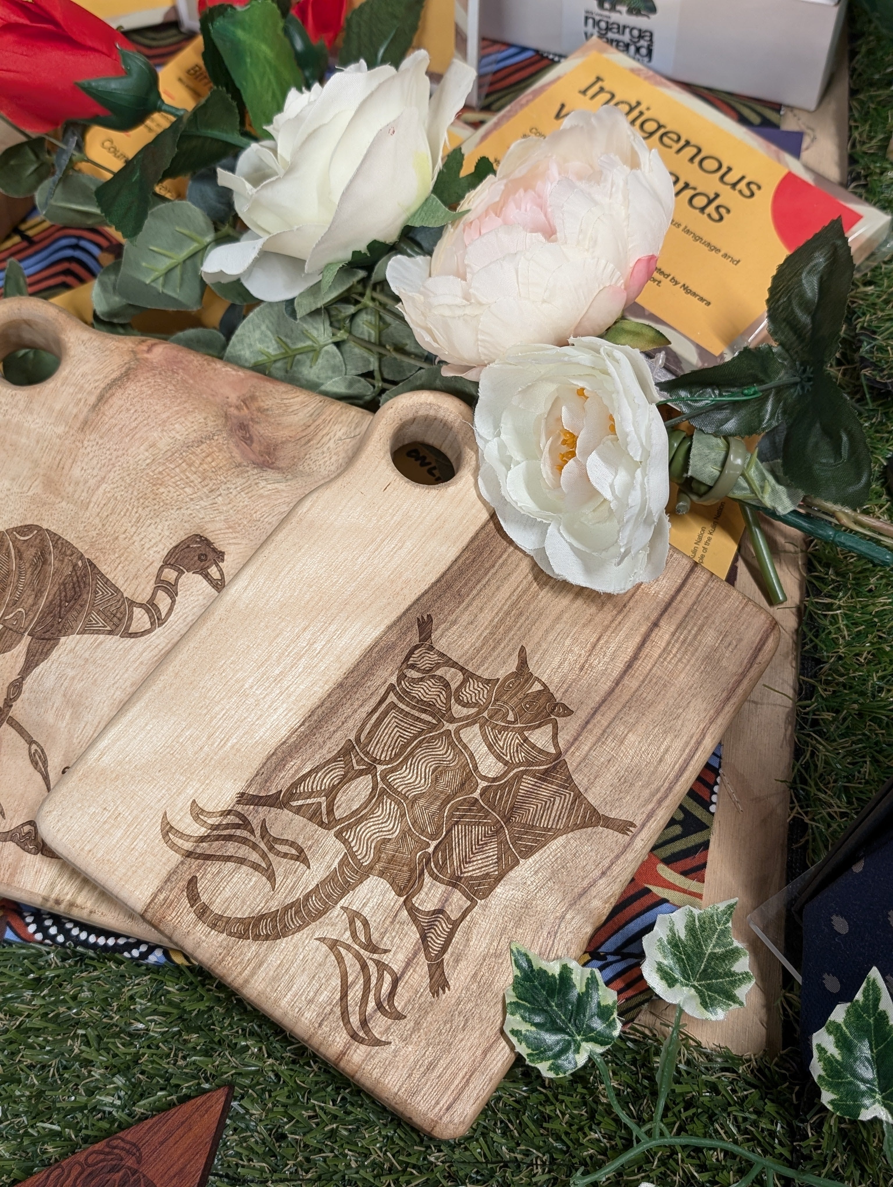 RMIT Store Camphor Laurel Board Extra Mini Rectangle with an intricate engraving of Durnong the Possum Glider, framed by indigenous-inspired patterns, surrounded by colourful artificial flowers.