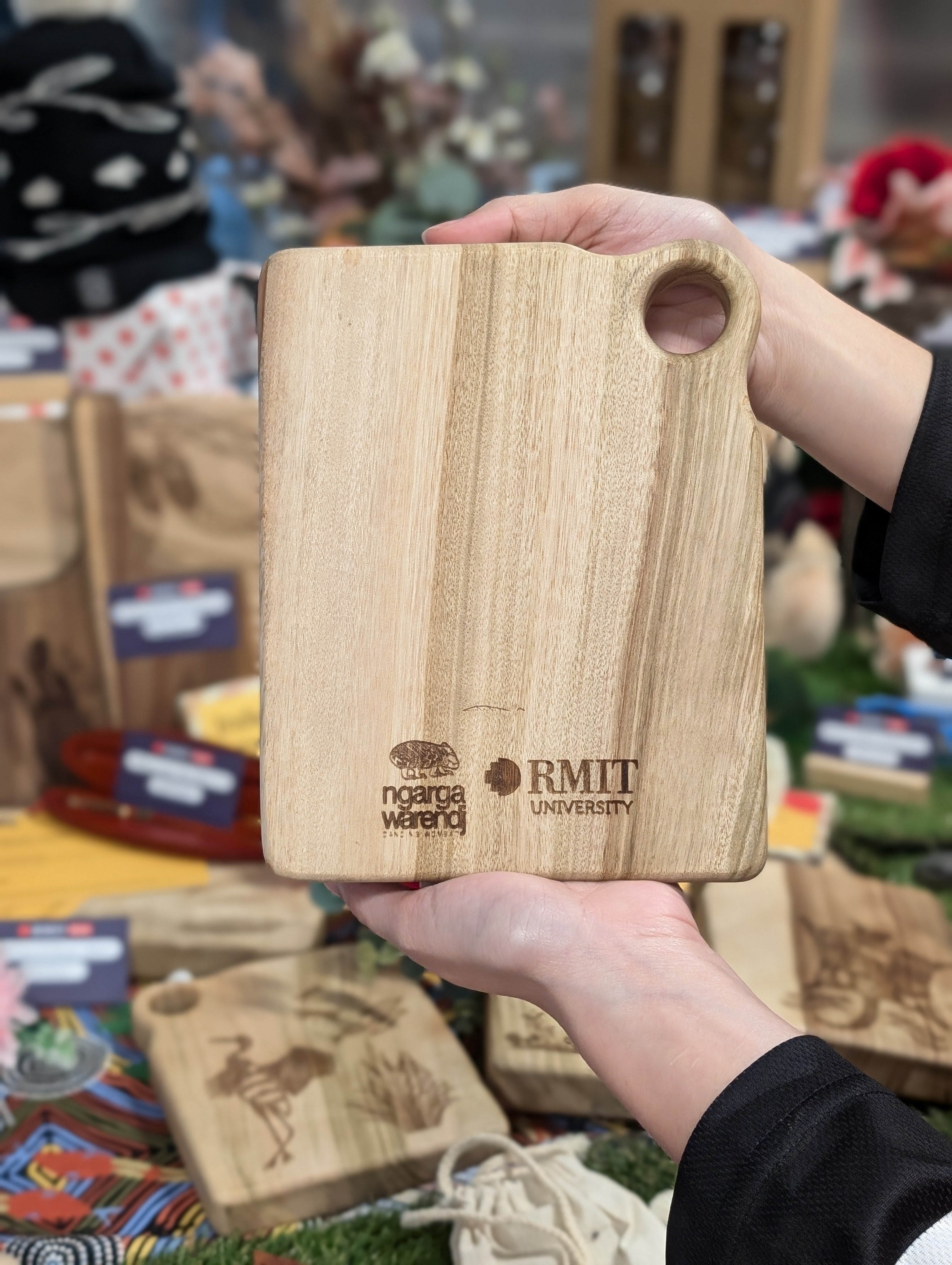 Reverse side of RMIT Store Camphor Laurel Board Extra Mini Rectangle, featuring the RMIT University and Ngarga Warendj logos engraved at the base, highlighting the natural wood texture.