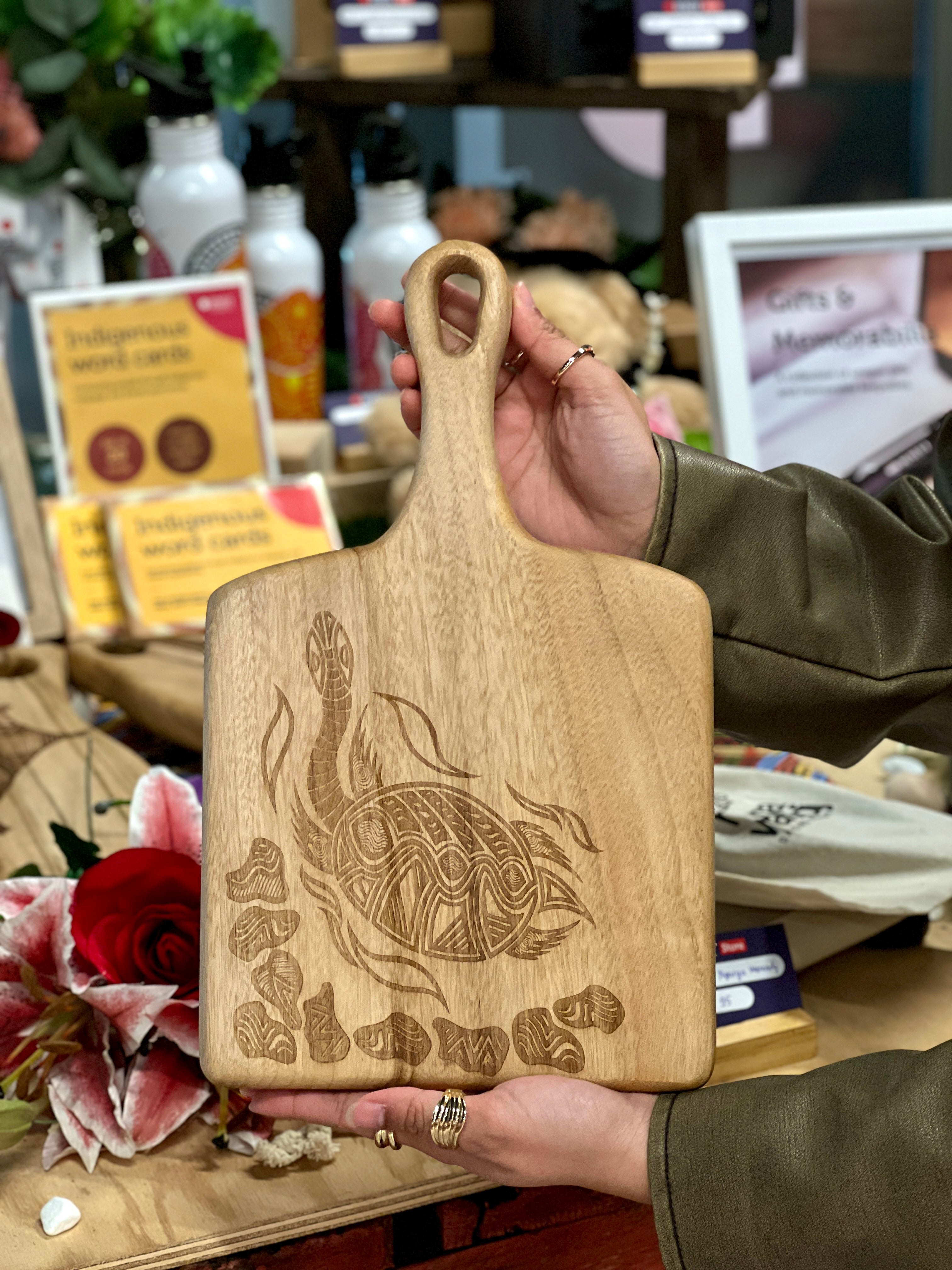 RMIT Store Camphor Laurel Square Paddle with an engraved Indigenous turtle design. Crafted from natural wood, this paddle features detailed carvings and vibrant flora, and offers a unique blend of artistry and functionality.