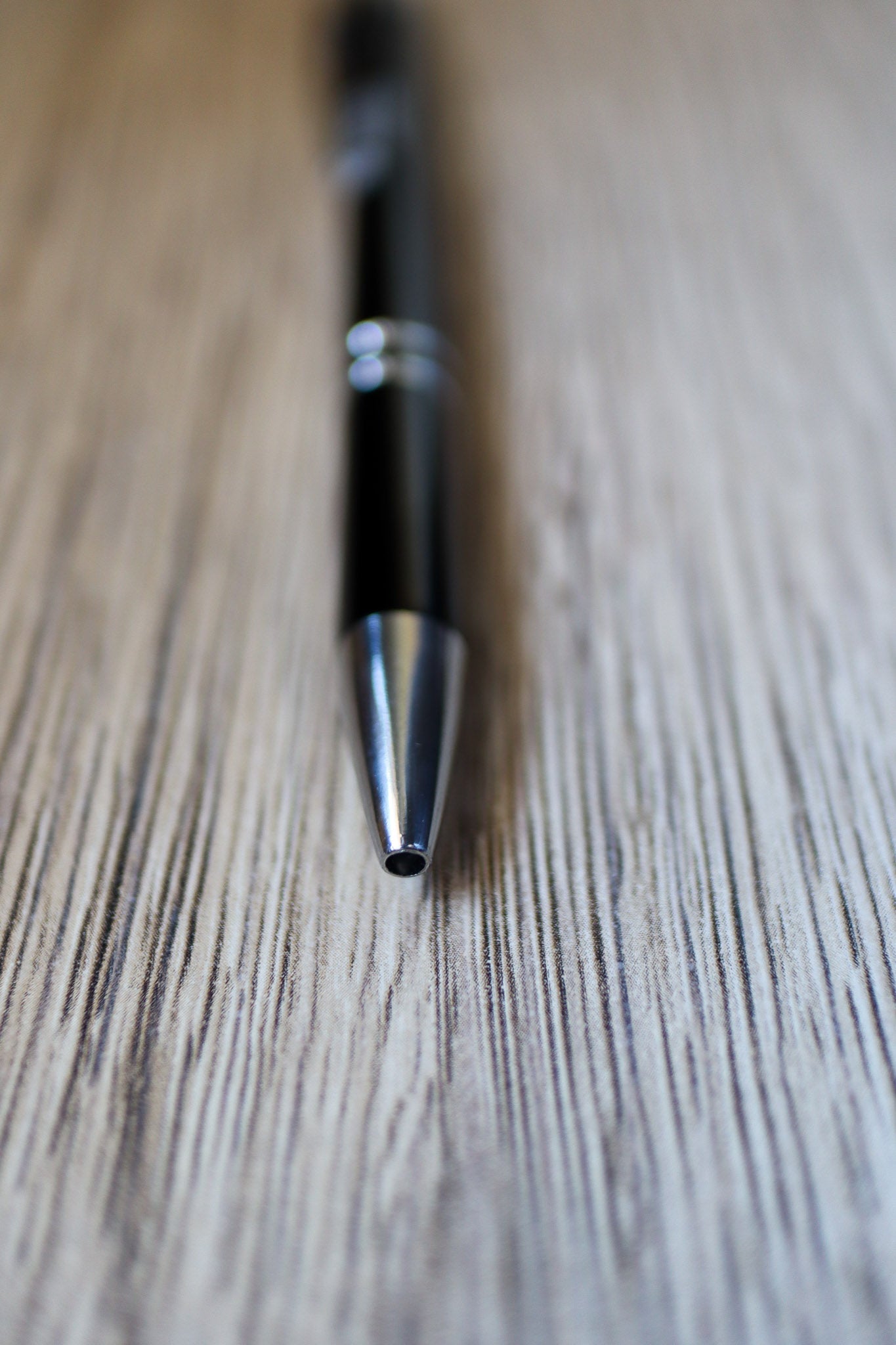 Close-up view of the black Classic Pen showing the pointy tip, resting on a wooden floorboard surface. Available at the RMIT Store.
