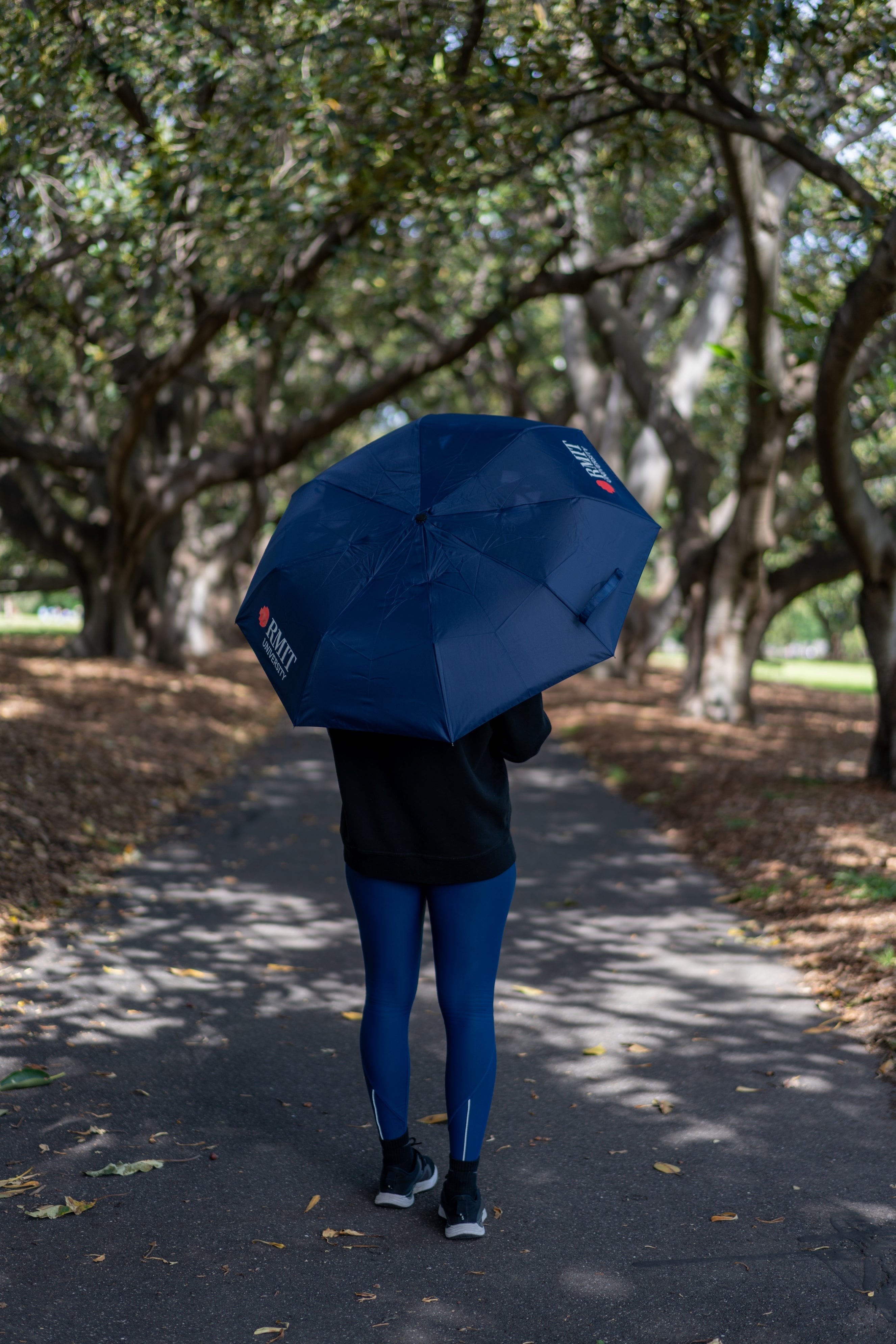 The RMIT Stgore Compact Umbrella in Navy opened up fully showing the twin RMIT University logos whilst being held by a model.