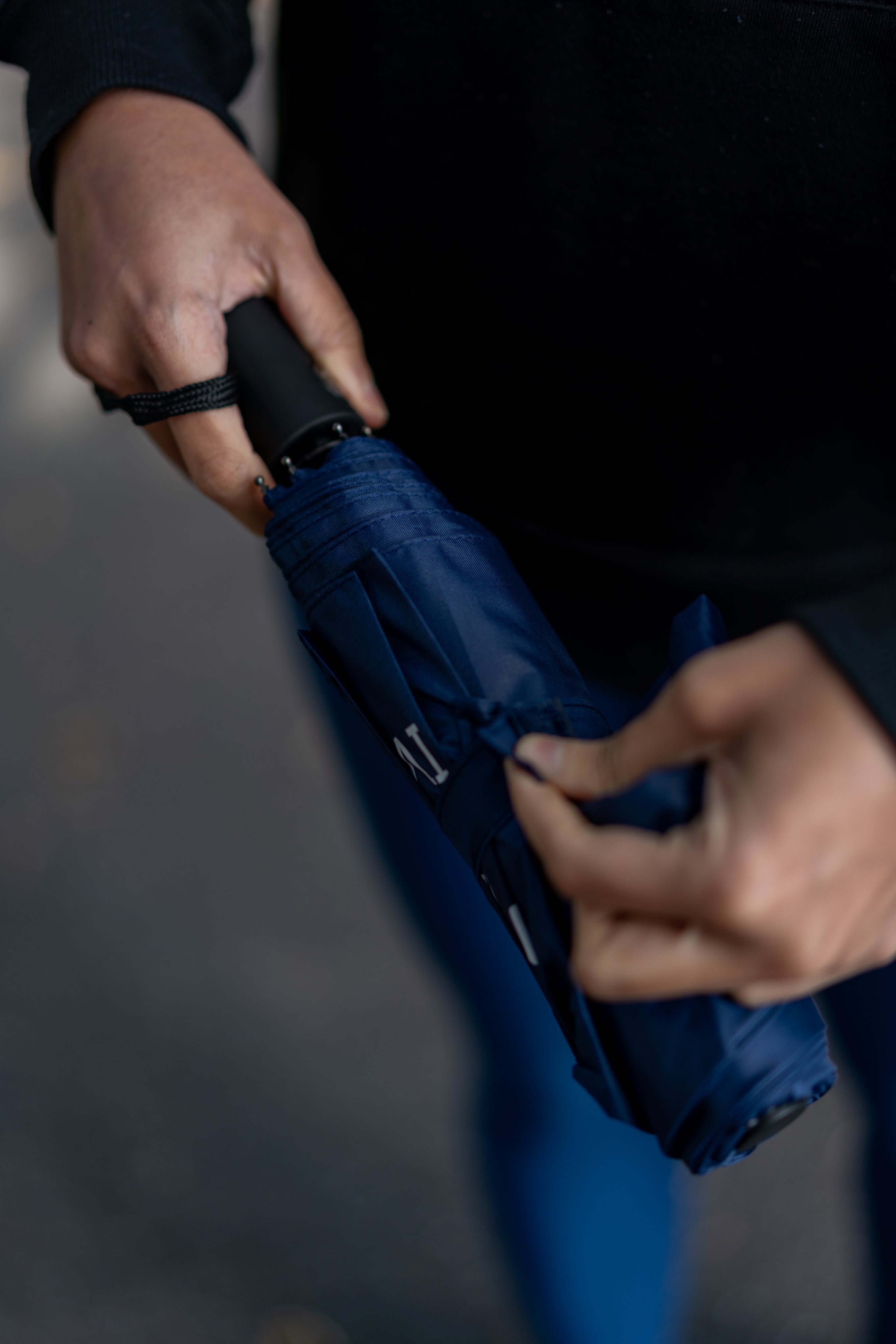 Model preparing to open an RMIT Store compact umbrella in navy blue, focusing on the handle and strap, ideal for easy carrying.