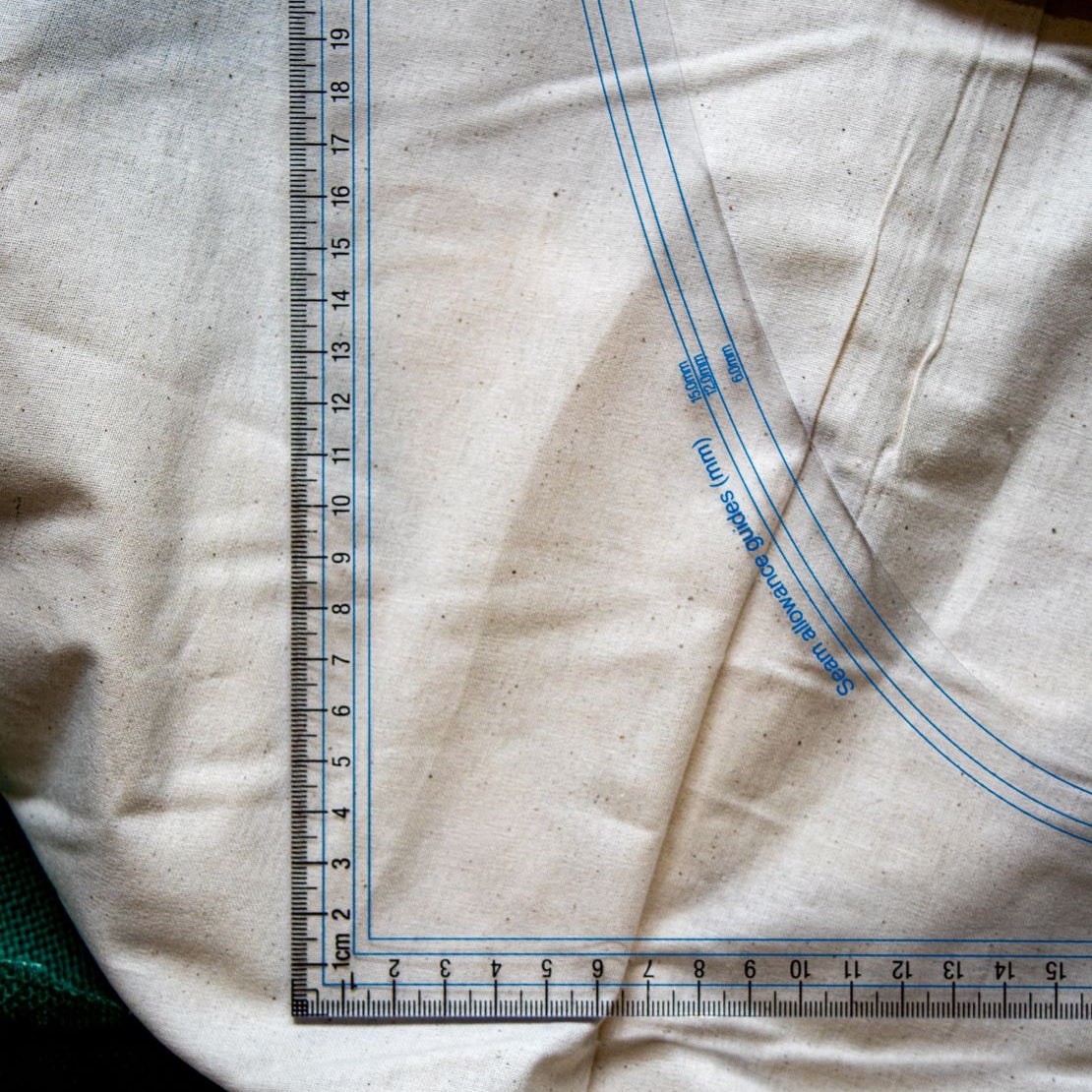 Close-up of the DM3 Graduated Set Square Ruler from RMIT Store showing detailed metric measurements and blue seam allowance guides on a beige textile.