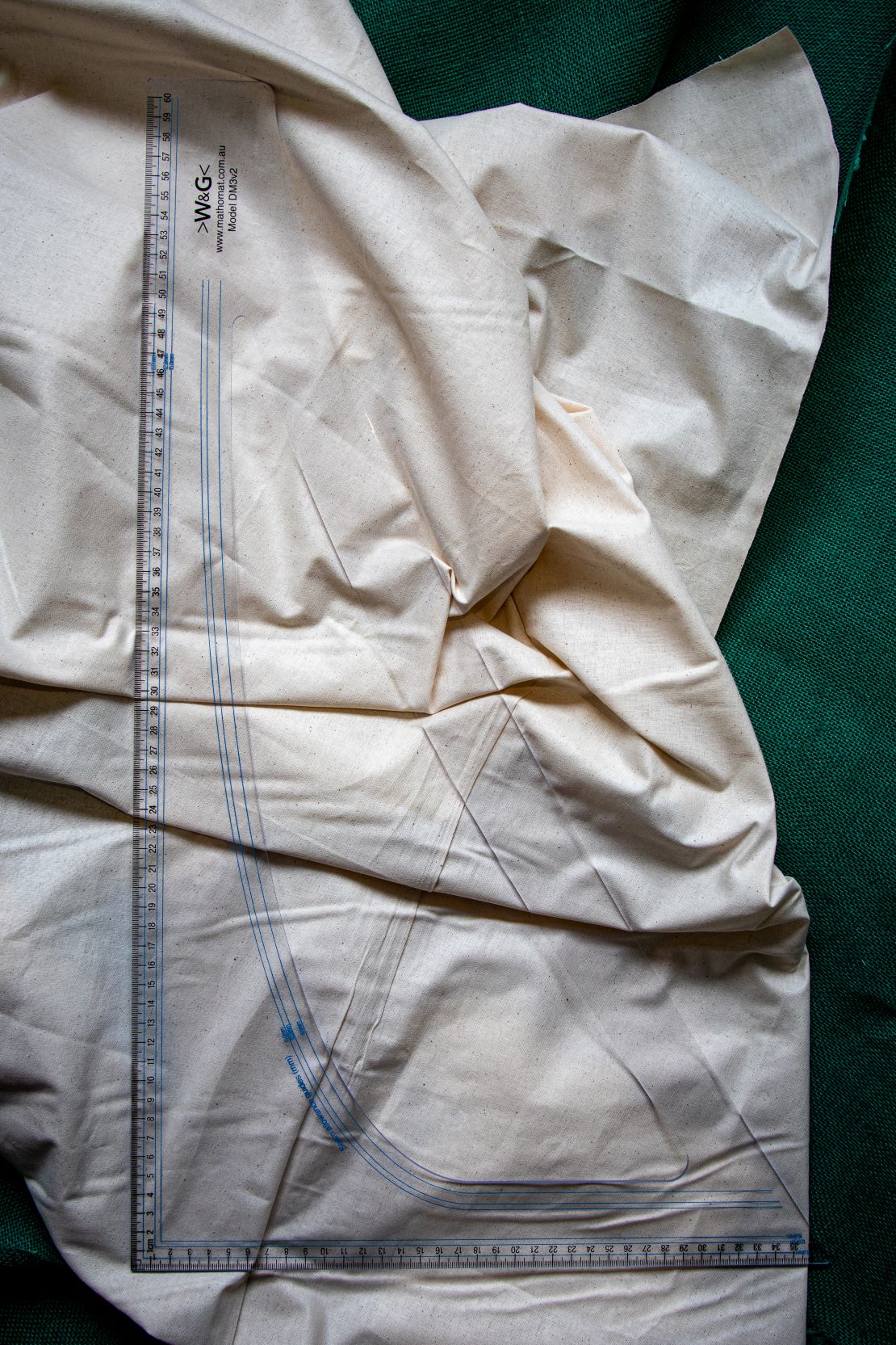 DM3 Graduated Set Square Ruler on beige fabric backdrop from RMIT Store. Features include clear plastic construction with precise metric markings along the edges and blue seam allowance guides.