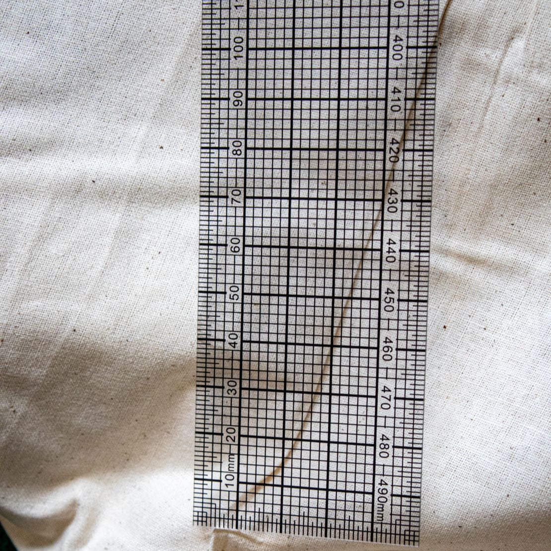 Close-up view of one end of the transparent DM7 grading ruler from the RMIT Store, showing detailed black measurement markings and curve guides against a beige fabric background.