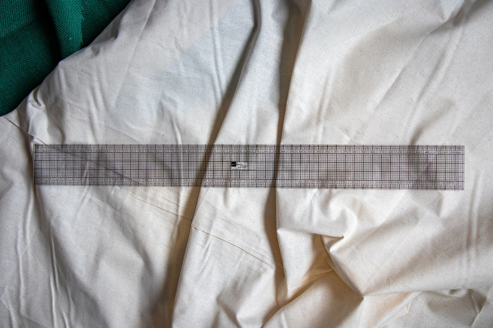 Full view of the transparent DM7 grading ruler from the RMIT Store, featuring clear black printed measurement lines and curve guides, displayed flat on a beige fabric surface.