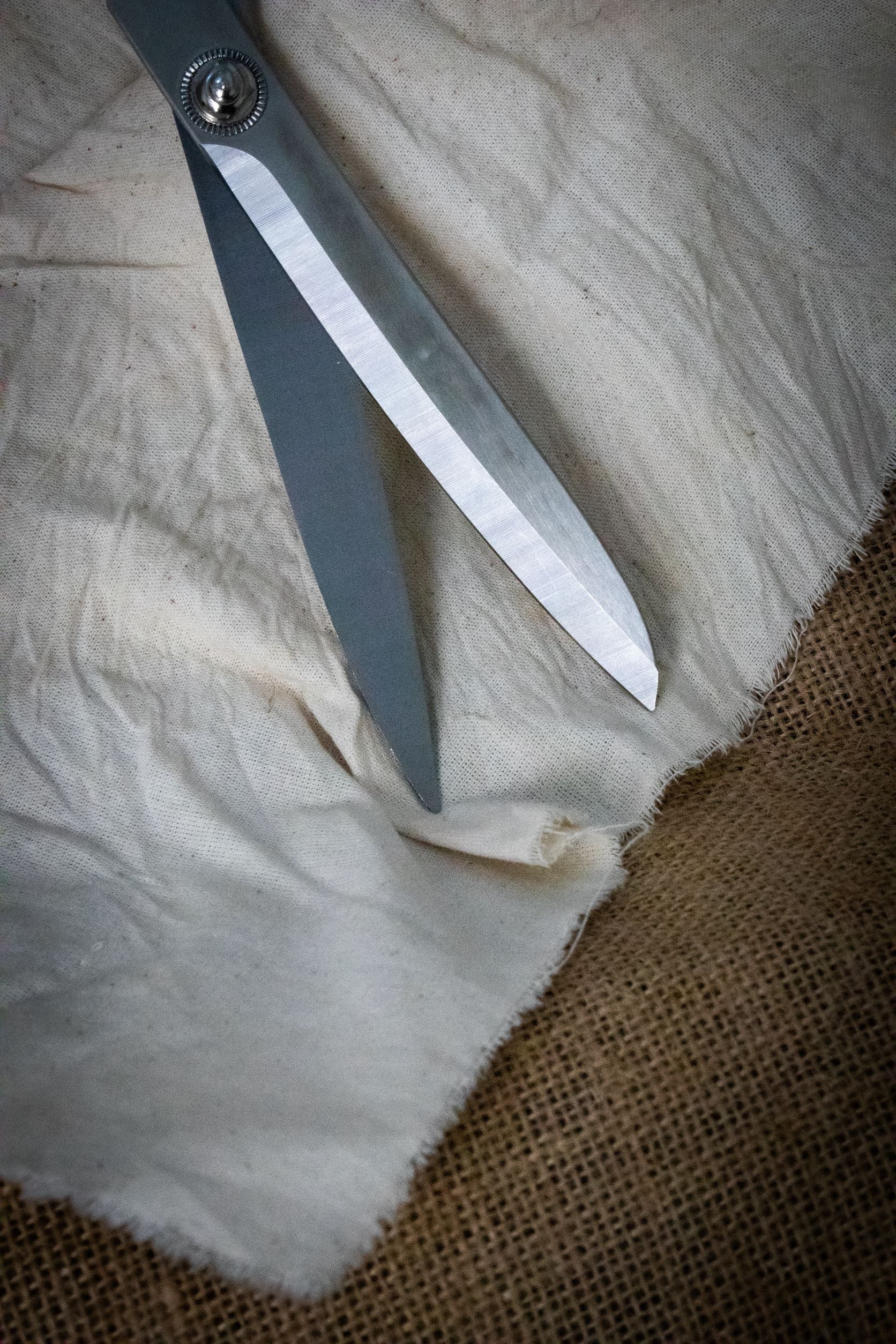 Close-up view of the Dress Making Scissors showing sharp stainless steel blades with a visible central screw joint, placed on a piece of light grey fabric.