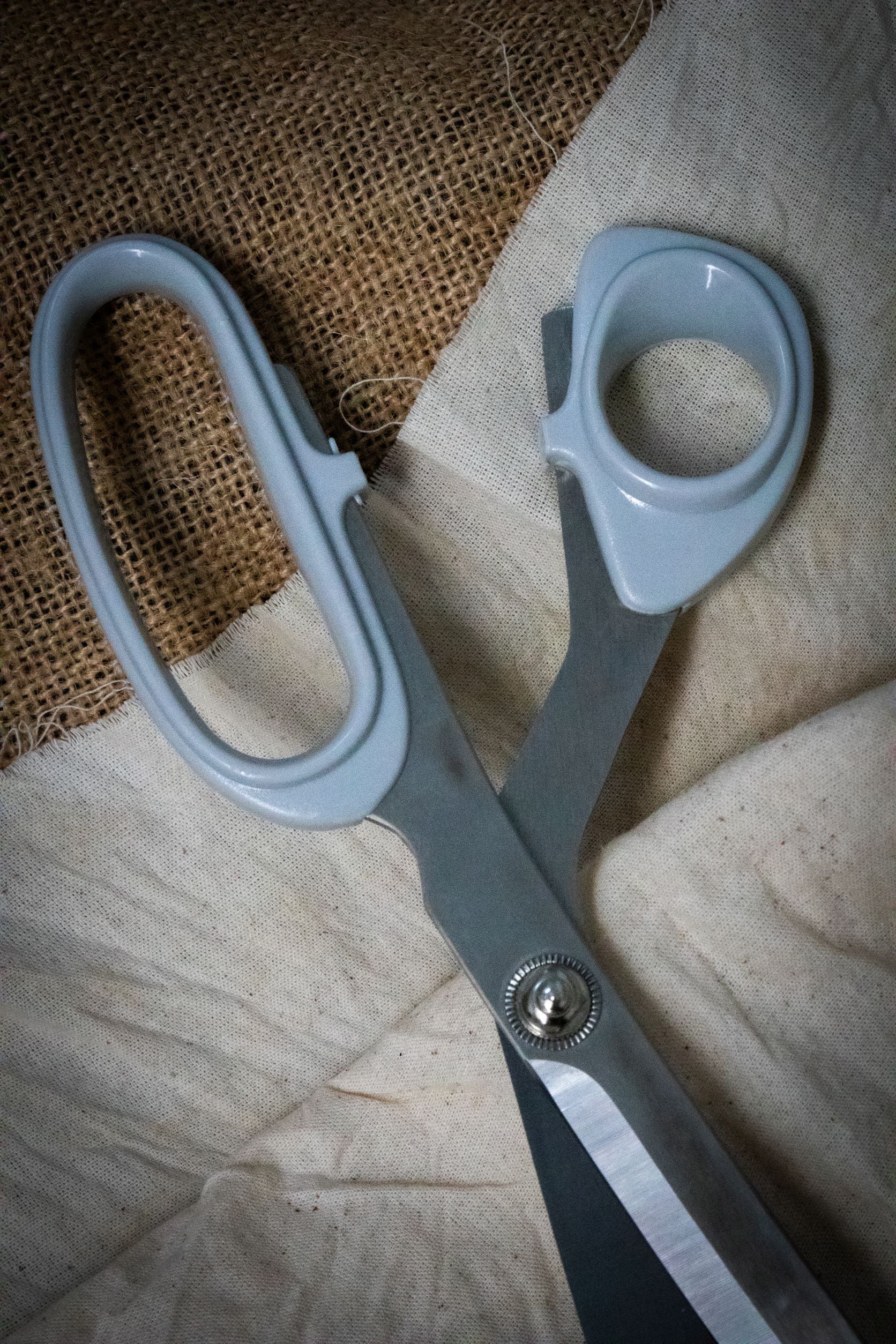 Full view of the Dress Making Scissors featuring long, sharp stainless steel blades and dark green ergonomic handles, positioned diagonally on a light grey surface. 