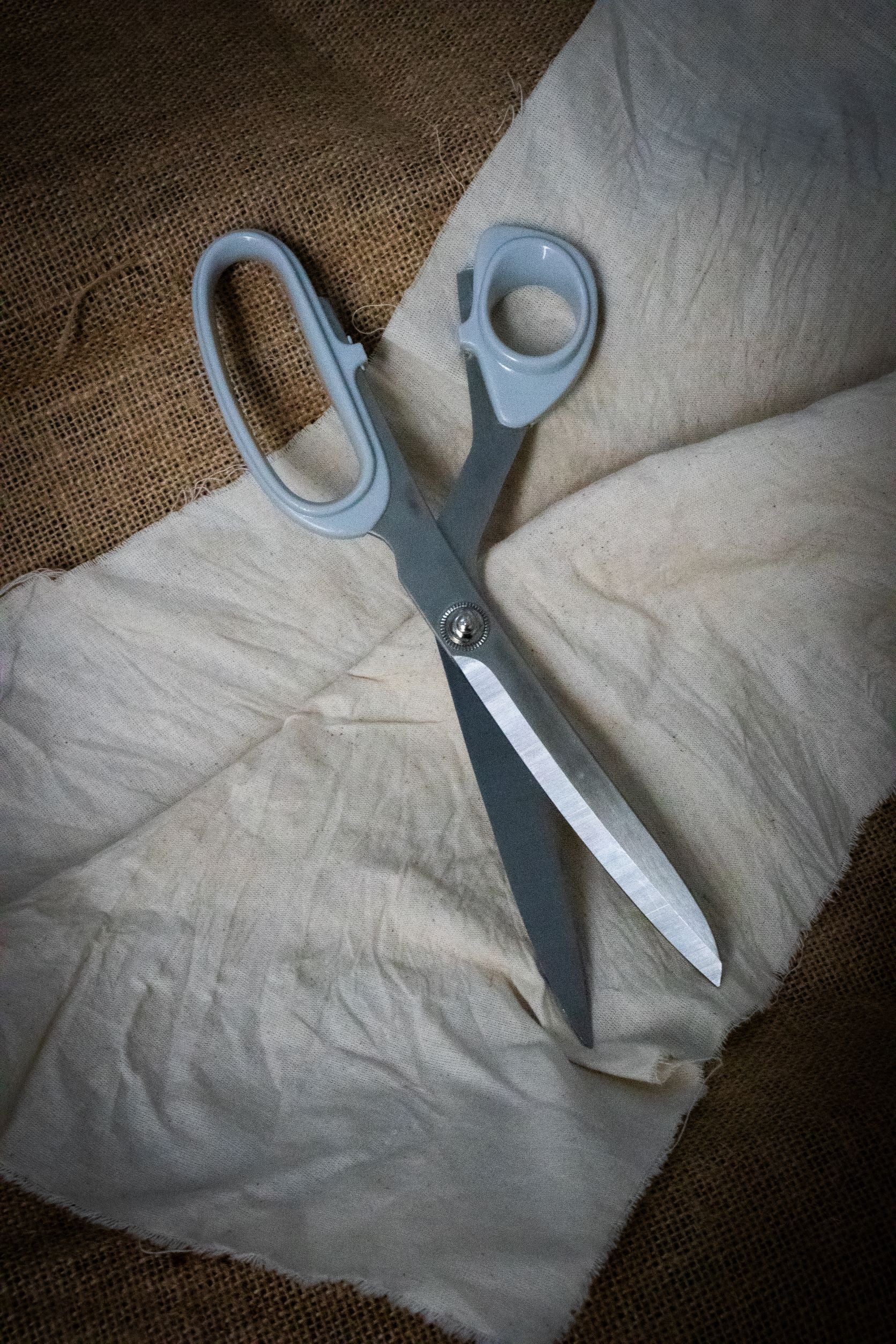 Full view of the Dress Making Scissors featuring long, sharp stainless steel blades and dark green ergonomic handles, positioned diagonally on a light grey surface. The central screw joint is visible. Available at RMIT Store.