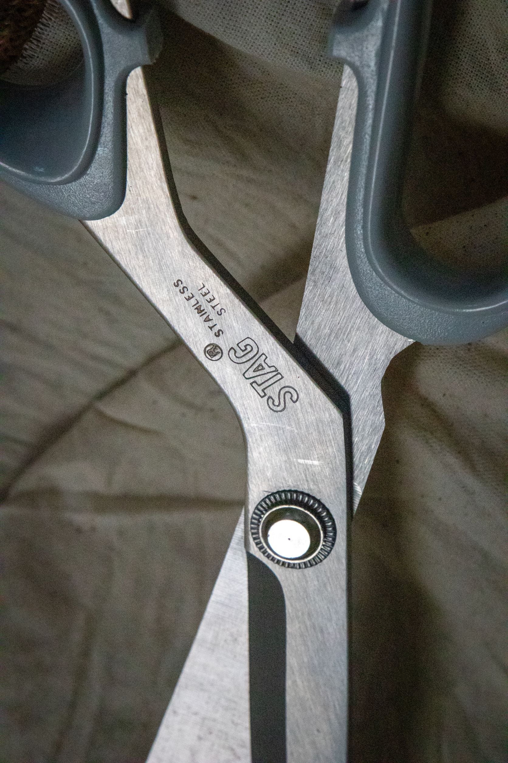 Close-up view of the Dress Making Scissors focusing on the central joint section, showing the metallic finish and polished surface with visible screw detail. Displayed on a grey surface. Available at RMIT Store.