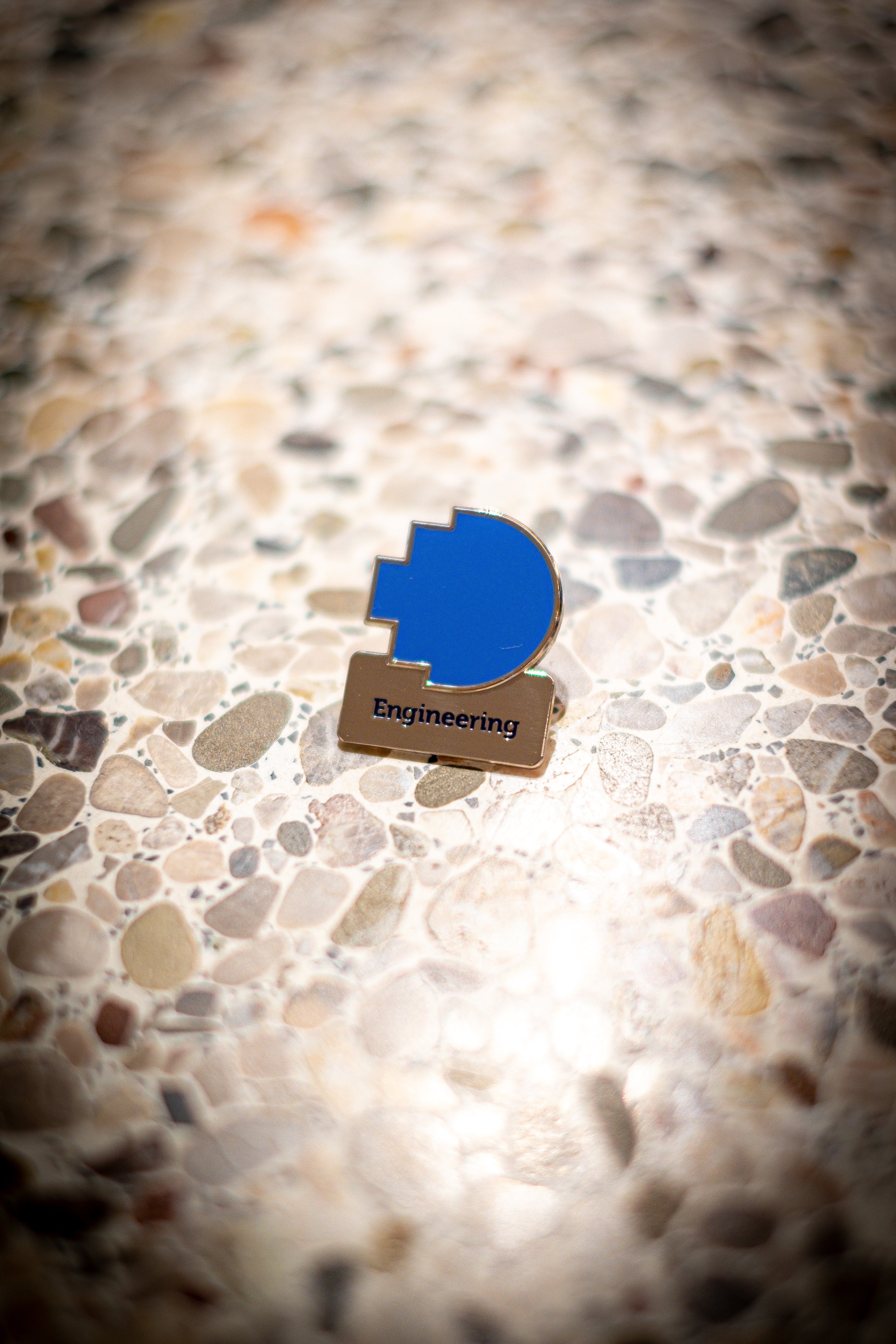 Engineering discipline pin featuring a blue pixelated logo above a silver square with 'Engineering' text, placed on a light marble background, available at the RMIT Store.