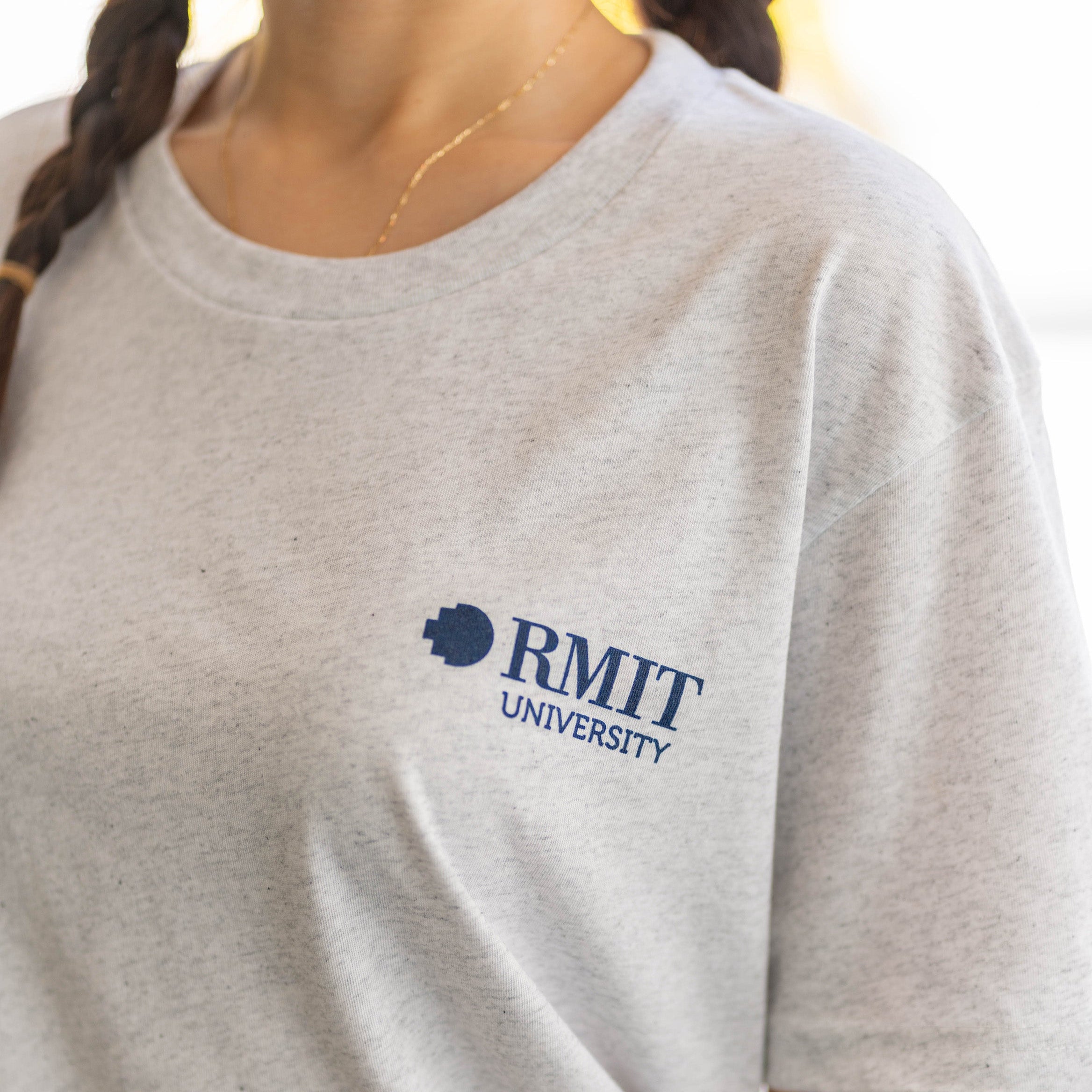 Model wears RMIT Essential Tee in white marle, showcasing a close-up of the navy blue RMIT University logo on the chest. Available at the RMIT Store.