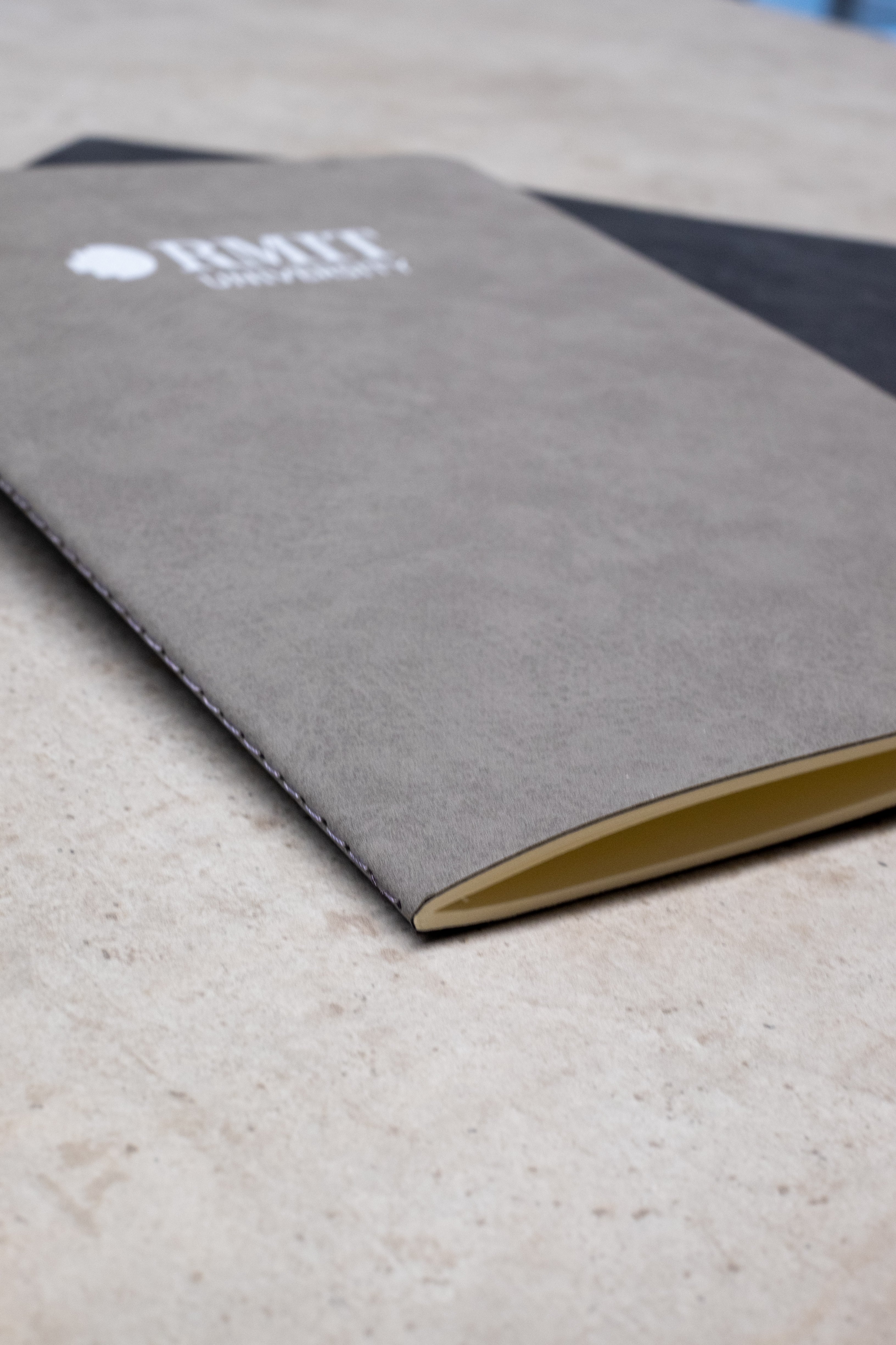 Grey Everyday Notebook from the RMIT Store with a soft-touch cover, featuring the white RMIT University logo, displayed closed on a light surface.
