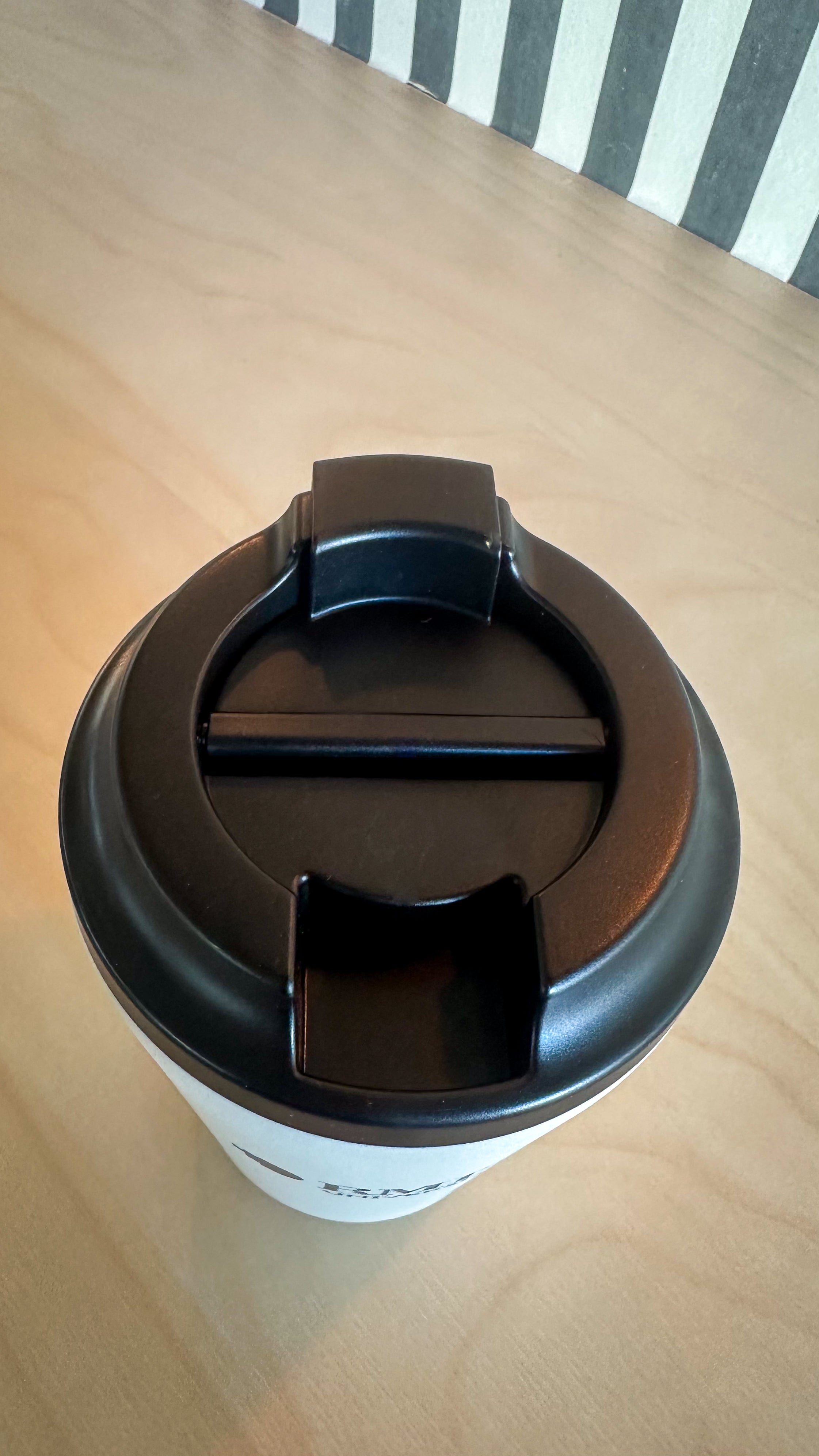 Top-down detail view of the Frost Everyday Reusable Cup by madebyFressko showing the black screw-top sip lid and drinking opening mechanism against a light timber tabletop background, available at the RMIT Store.