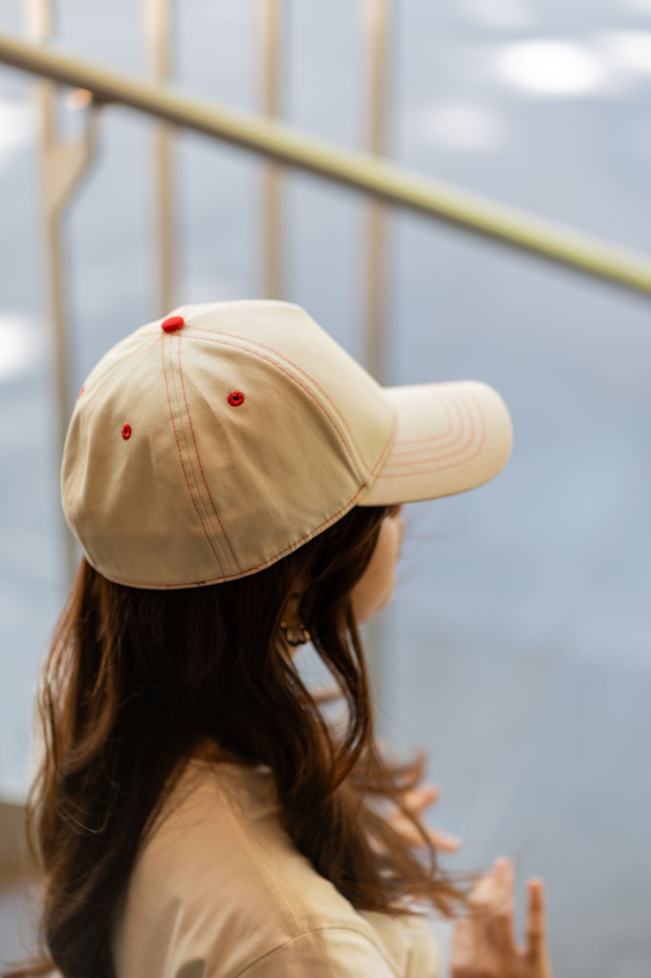 RMIT Store flex fit cap in light beige, highlighted by red stitching, worn by a model with flowing hair. Captured indoors with soft lighting, emphasising modern casual style.