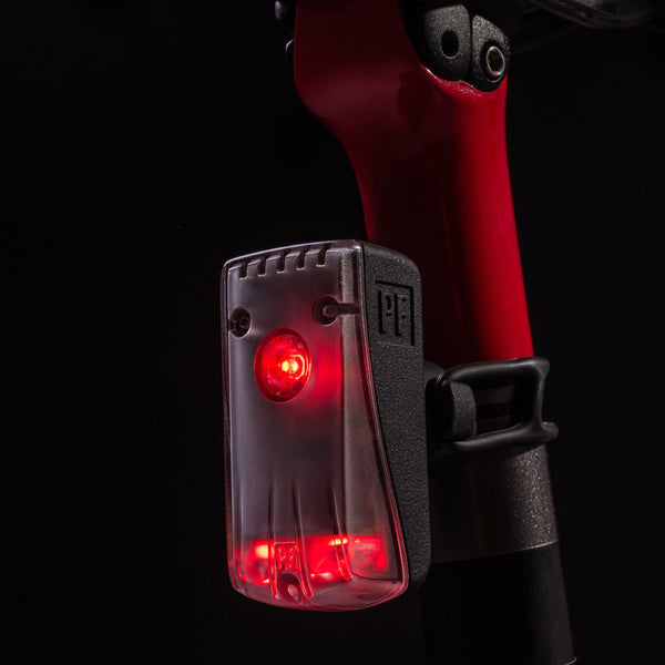 Close-up of the RMIT Store Flock Light in the dark, featuring a compact rectangular design with a black front cover and casing, flashing a bright red safety light.