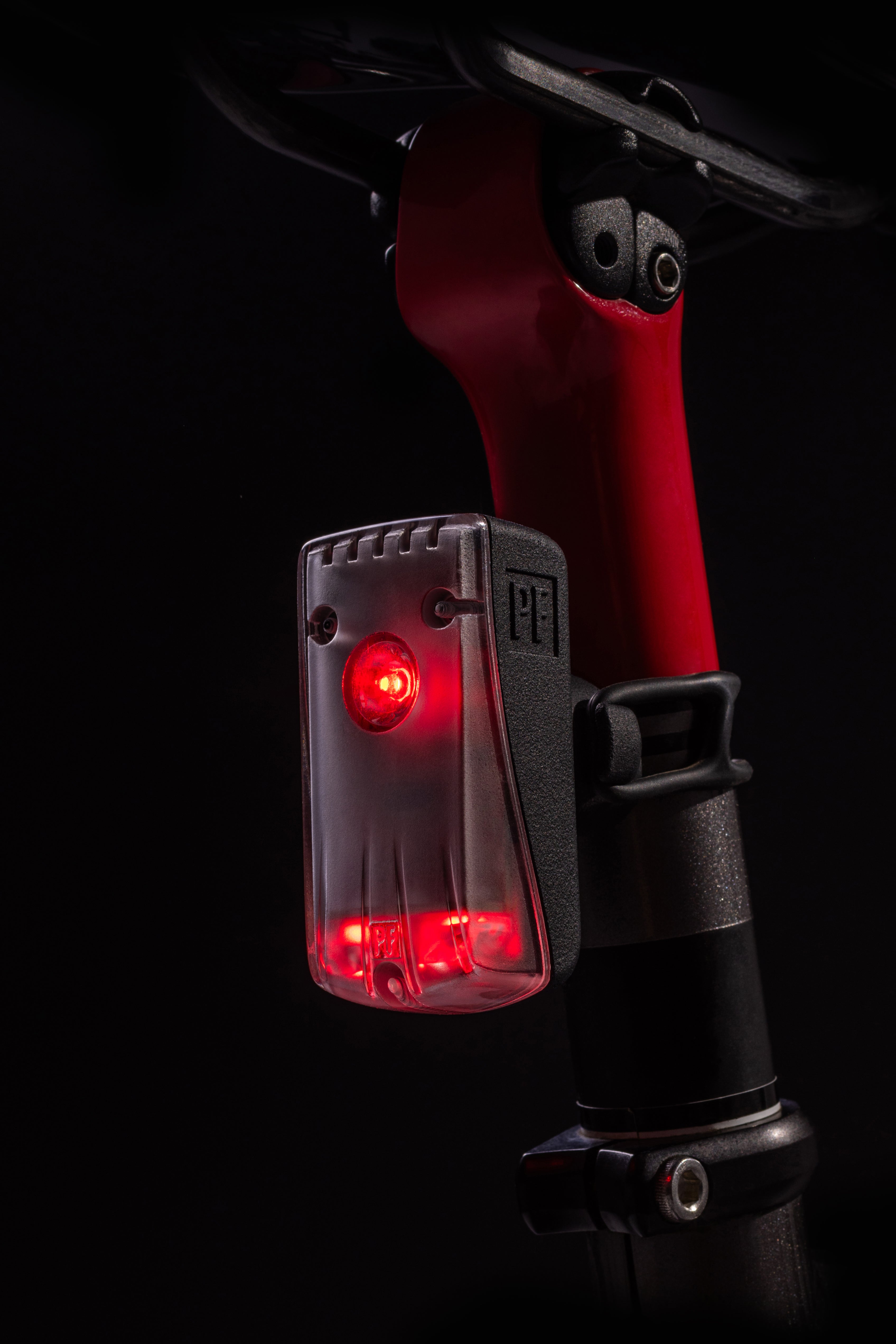 Close-up of the RMIT Store Flock Light in the dark, featuring a compact rectangular design with a black front cover and casing, flashing a bright red safety light.