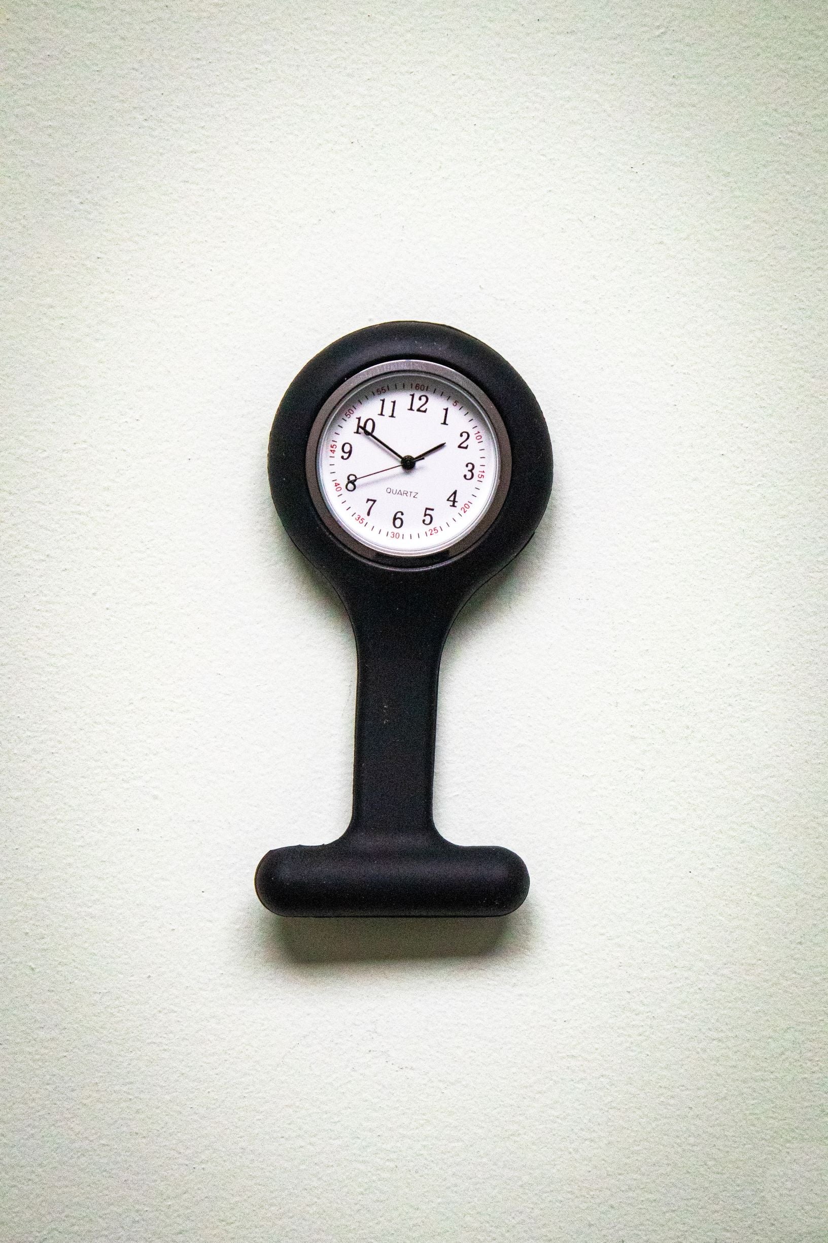 Upside-down front view of the RMIT Store black fob watch, showing a white clock face with black numerals and three black hands inside a black silicone casing. 