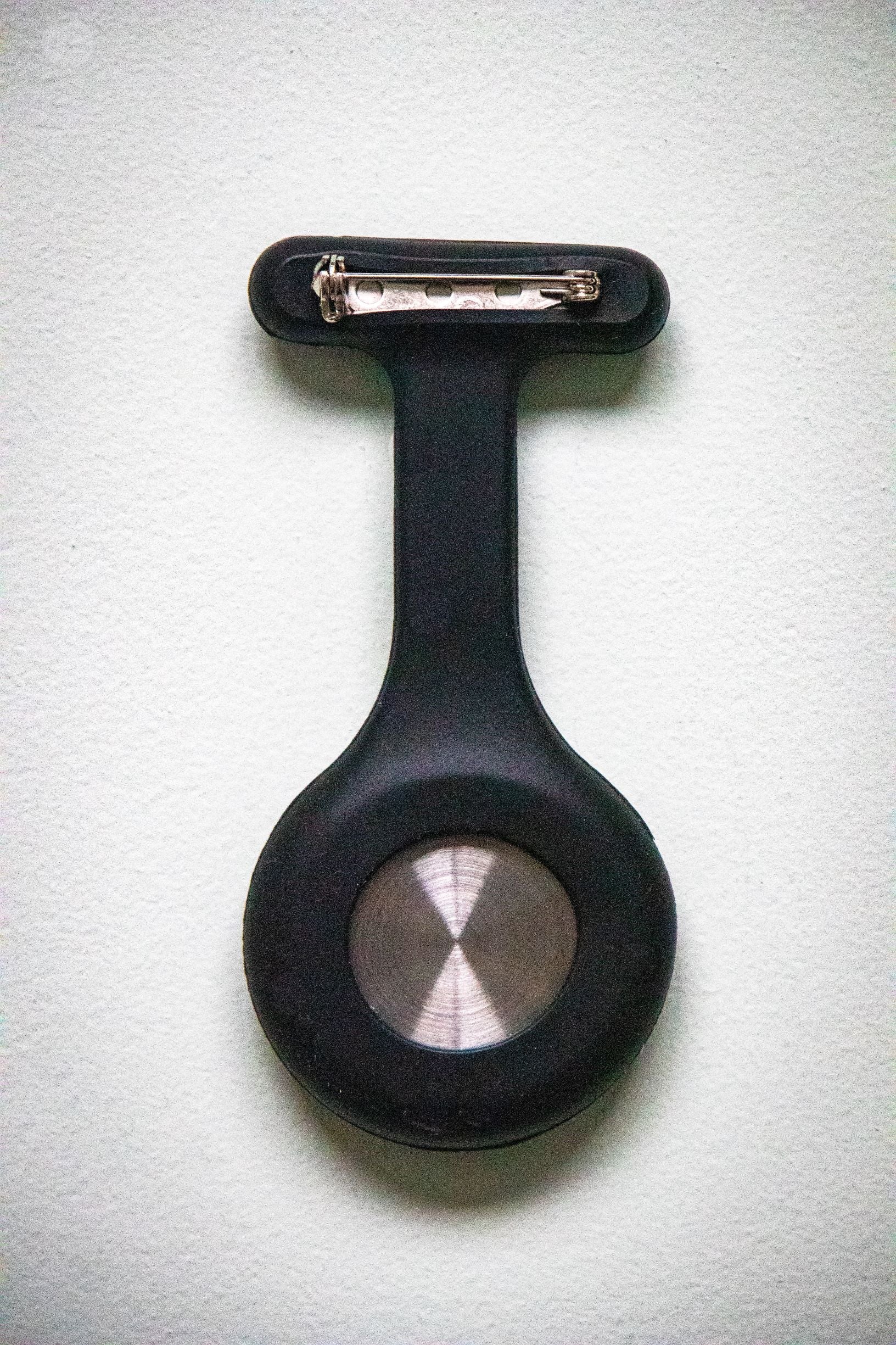 Rear view of the RMIT Store black fob watch, showing a matte black silicone casing with a silver pin clasp attachment.