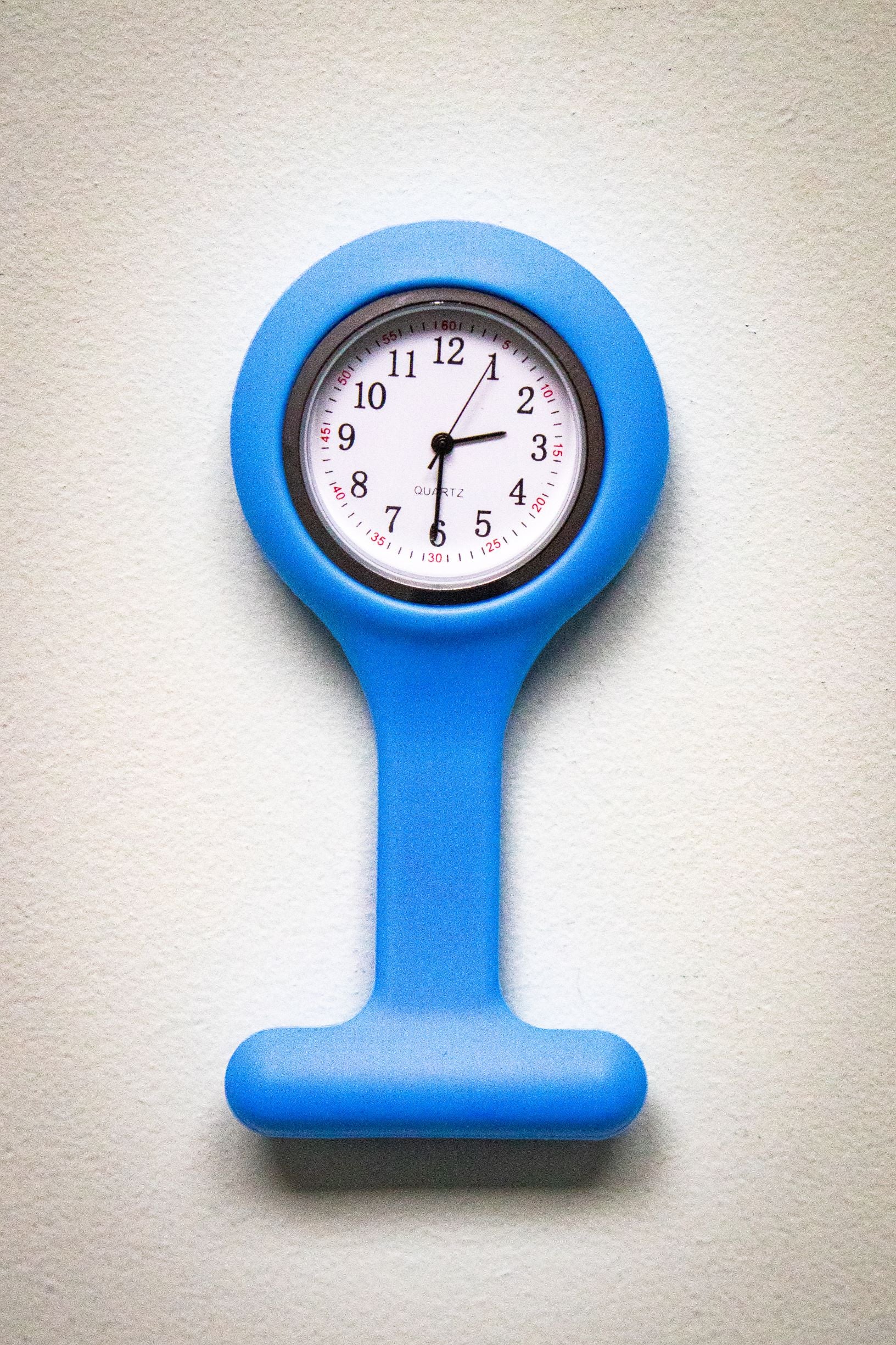 Upside-down front view of the RMIT Store light blue fob watch, with a clear white clock face, black numbers, and three black hands, set in a silicone casing.