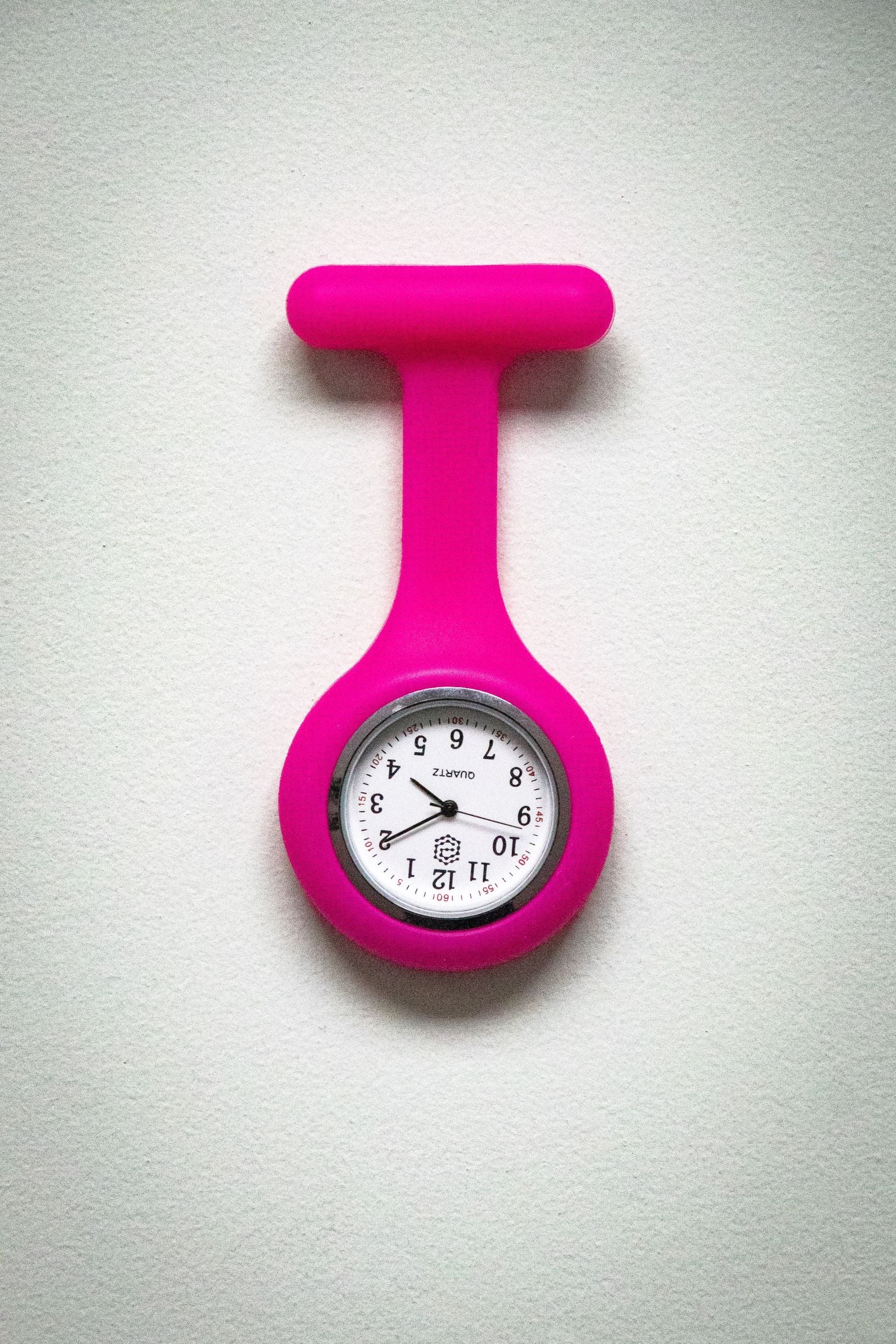 Front view of the RMIT Store magenta fob watch showing a white clock face with black numbers and three black hands inside a magenta silicone casing.