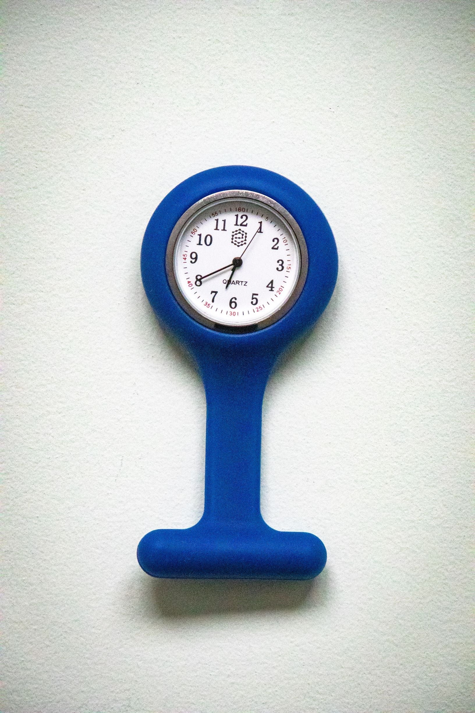 Front view of the RMIT Store navy fob watch placed upside down, showing the white clock face with black numbers and three black hands within a navy silicone casing. 
