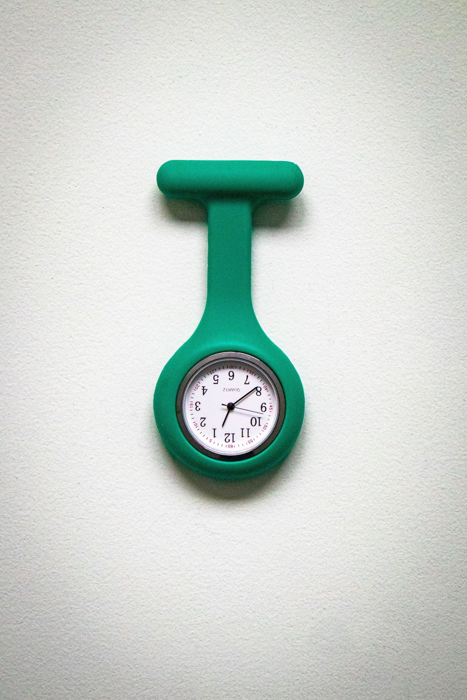 Front view of the RMIT Store teal fob watch, showing a white clock face with black numbers and three black hands, housed in a teal silicone case.