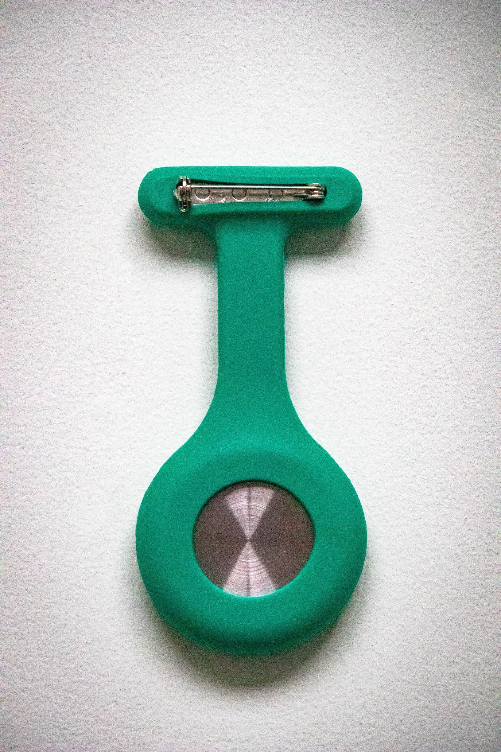 Rear view of the RMIT Store teal fob watch, featuring a smooth teal silicone casing and a silver pin clasp attachment.