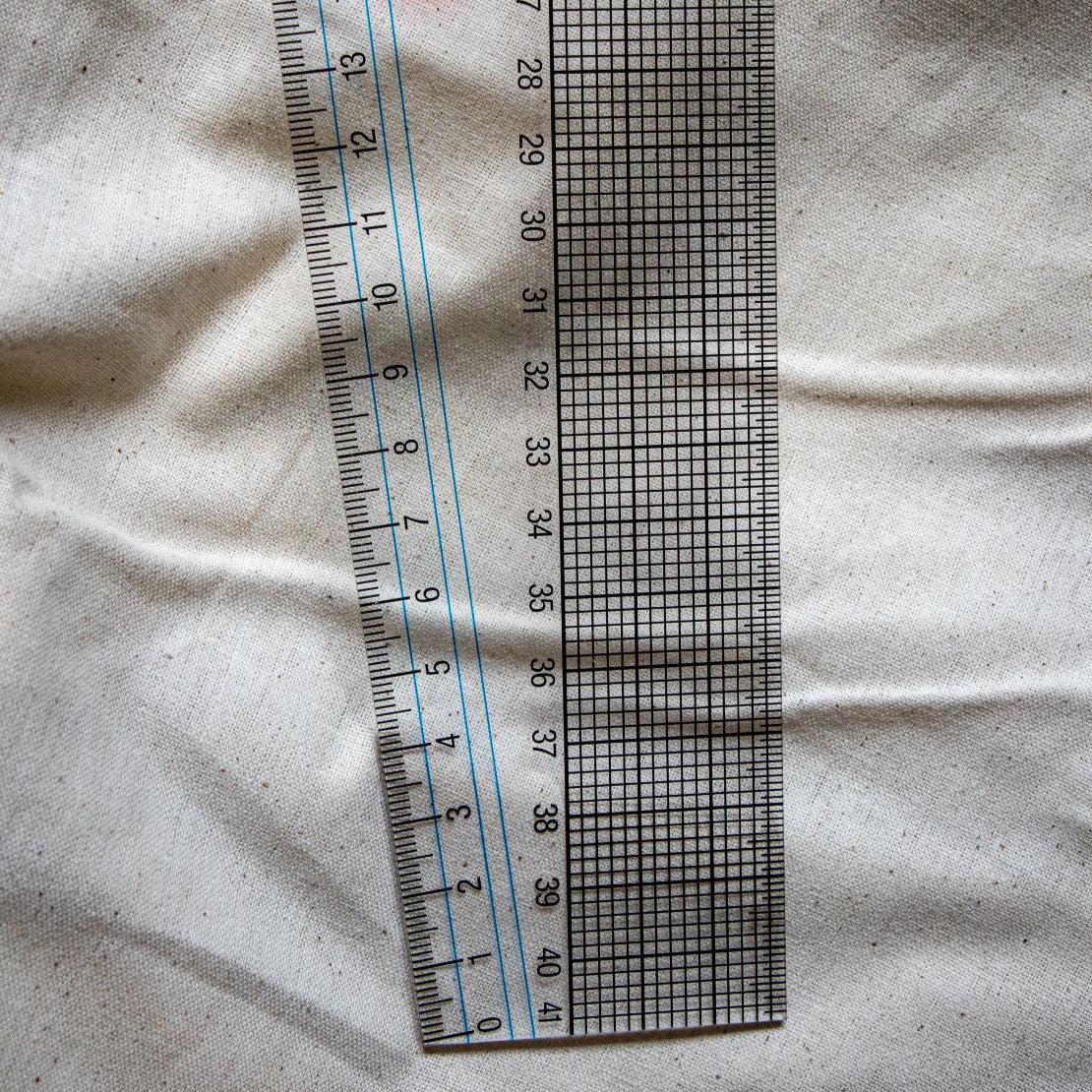 The bottom view of a clear plastic French curve ruler with printed black measurement markings and gridlines, featuring curved and angled edges for pattern drafting. Positioned flat on a light beige surface, available from the RMIT Store.