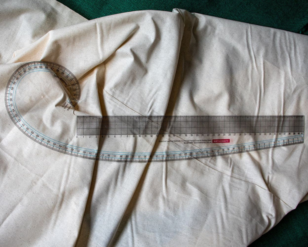 Clear plastic French curve ruler laid flat on a light beige surface, showing full view with black printed measurement markings and curved design edges. Available from the RMIT Store.