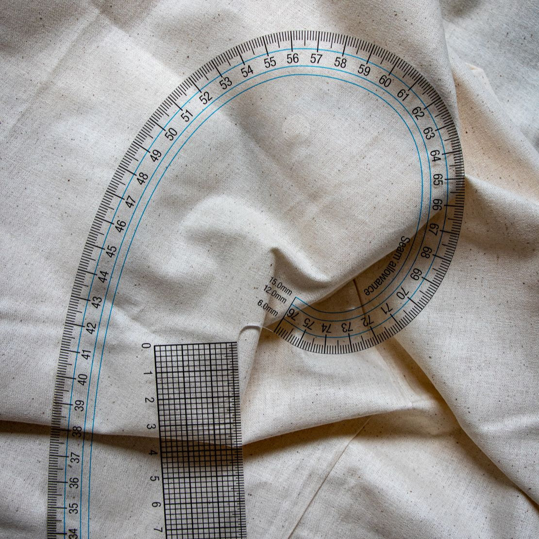 Clear plastic French curve ruler showing the top section, featuring black printed measurement markings and gridlines on curved edges, photographed at an angle on a light beige surface. Available from the RMIT Store.