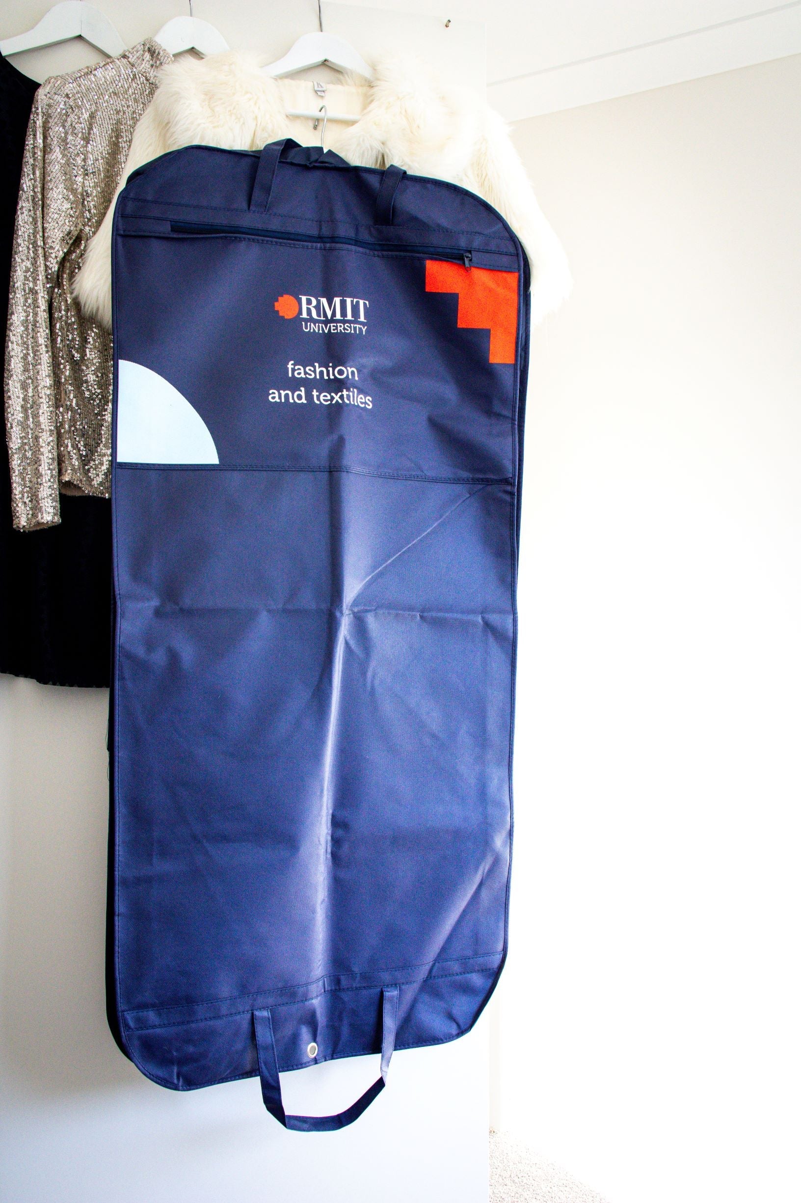 Full rear view of the RMIT Garment Bag in navy, displaying the "RMIT University" logo in white and red at the top, with the words "Fashion and Textile" written underneath in white text. The bag is shown in its entirety, highlighting the clean, simple design with a clear focus on the logo and text.