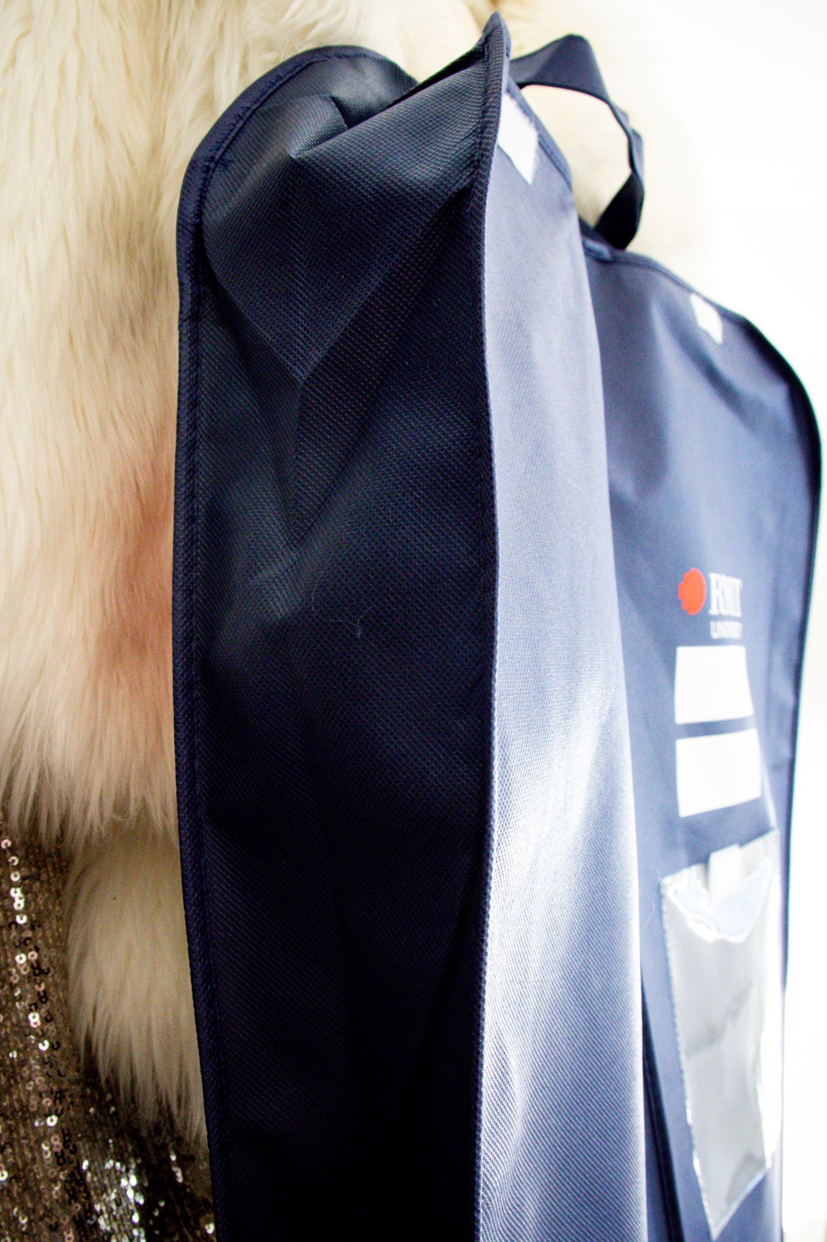Side view of the RMIT Garment Bag in navy, hanging against a white wall. The bag features the “RMIT University” logo in white and red, with two blank white-labelled areas intended for writing, positioned near the top. 