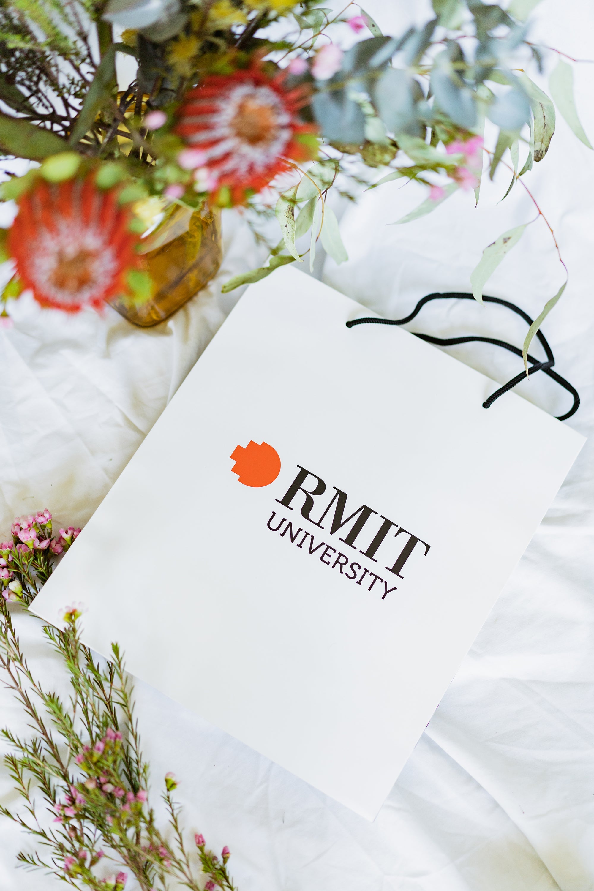 Top view of the RMIT Store gift bag laid flat, clearly showing the full RMIT University logo in red and white. The black string handle is visible against the bag’s matte white surface.