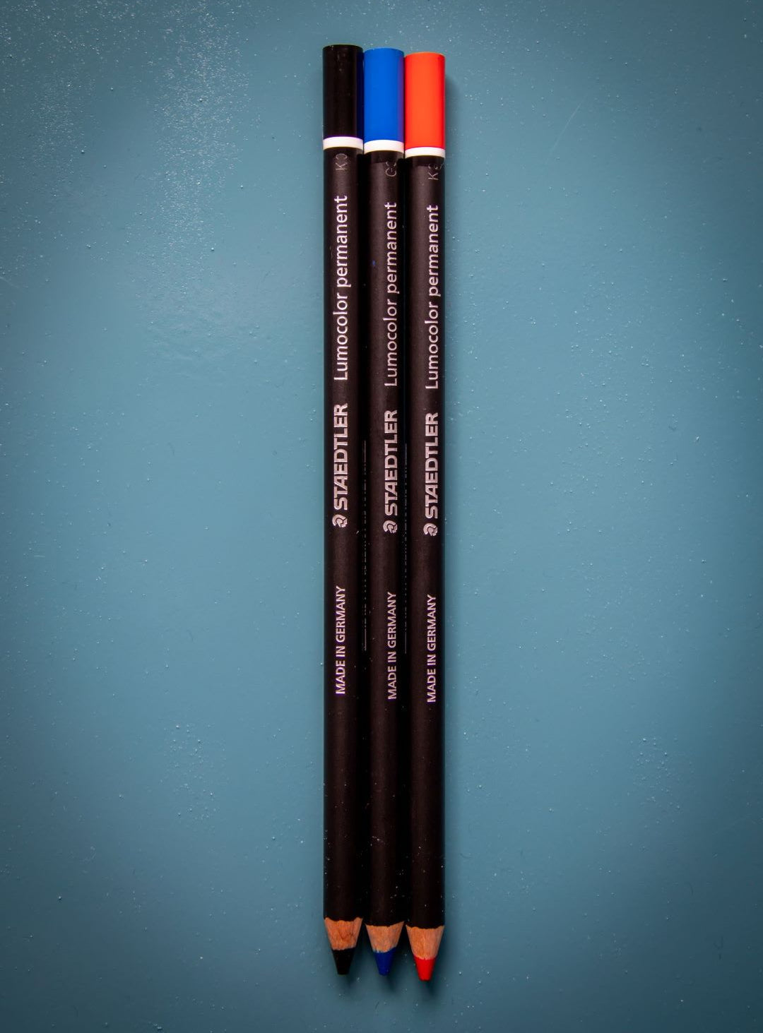 Trio of black, blue, and red Glasochrom dry markers from the RMIT Store, arranged neatly on a teal background, emphasising their vibrant colour and permanence.