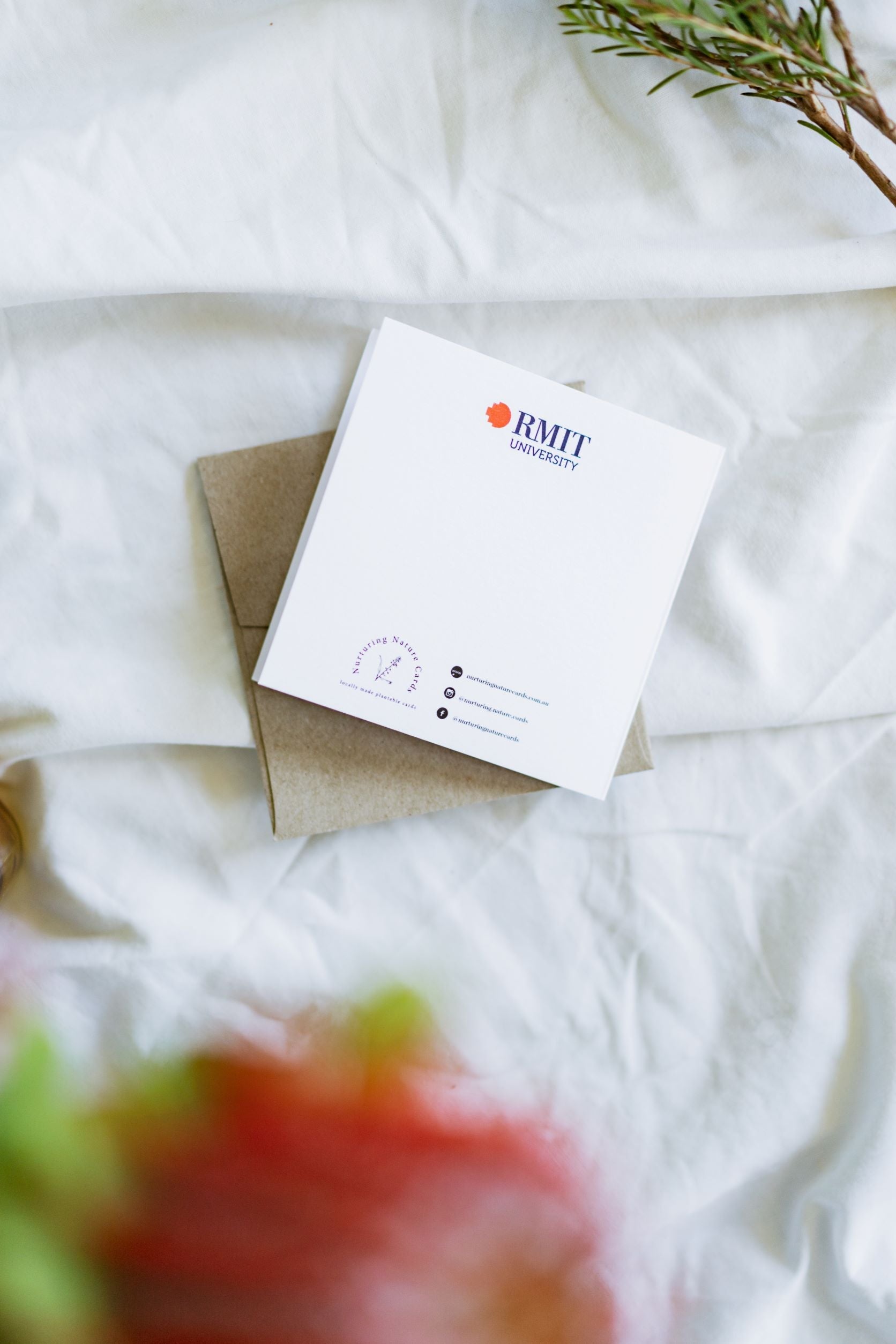 Rear view of the RMIT Store Graduation Congratulations card, unseeded version, laid flat on a light brown envelope against a white fabric background, showing the plain back surface with the RMIT University logo printed at the top.