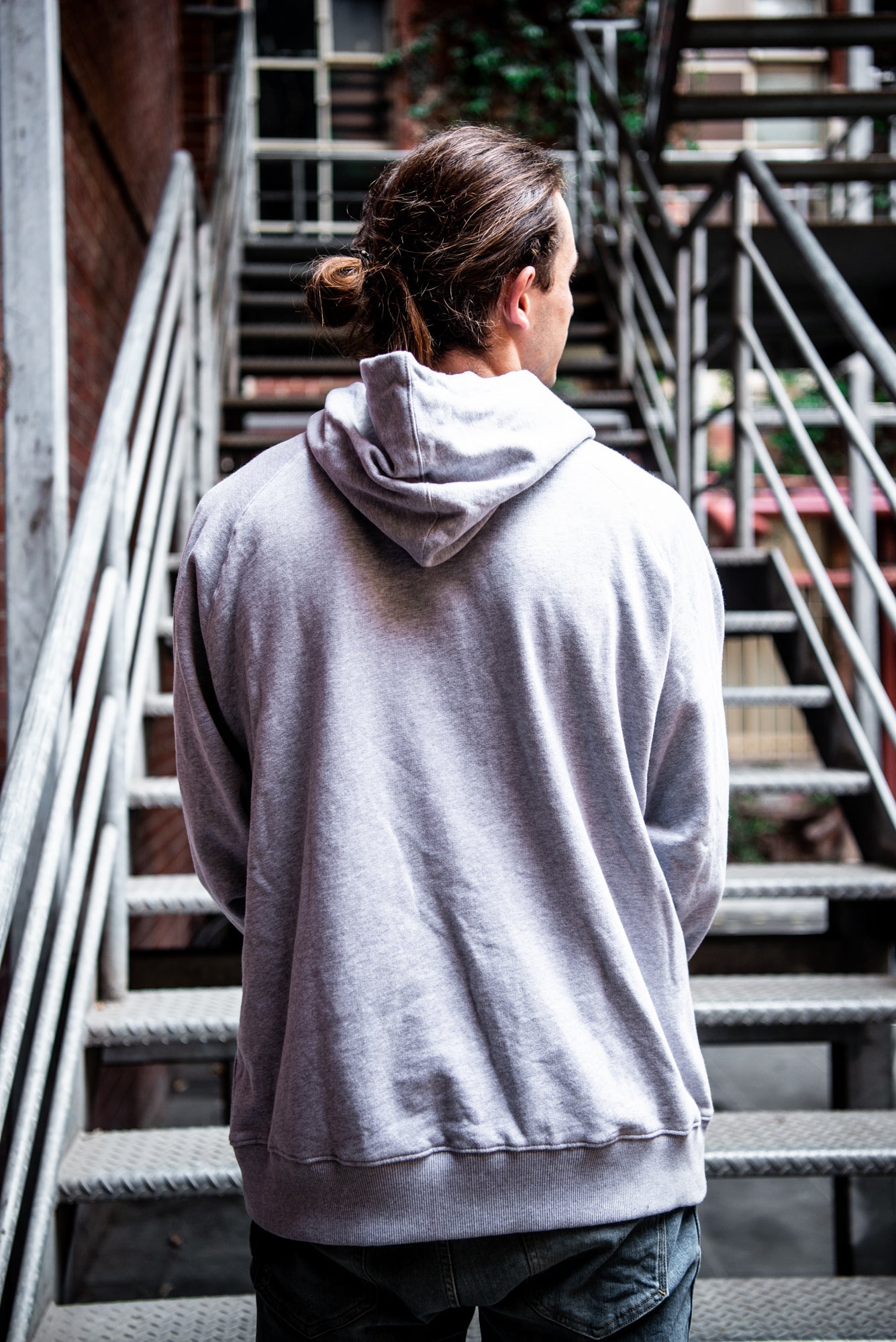 Rear view of a male model wearing a grey Fairtrade hoodie from the RMIT Store, showing the plain back with the hood down. The hoodie has a relaxed fit.