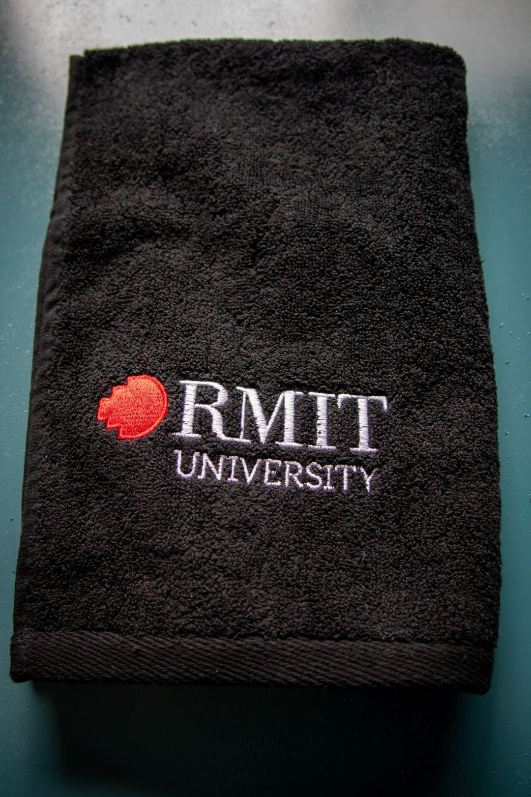 Folded RMIT Store hand towel neatly displayed with the "RMIT University" logo in white and red clearly visible on the front. 